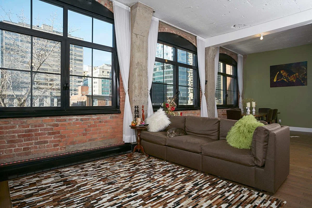 A real estate photo of a living room with a red brick wall and a cat sleeping on the couch.