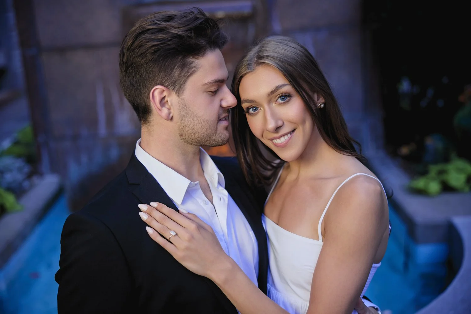 A portrait of a young man and woman in front of a fountain at night.