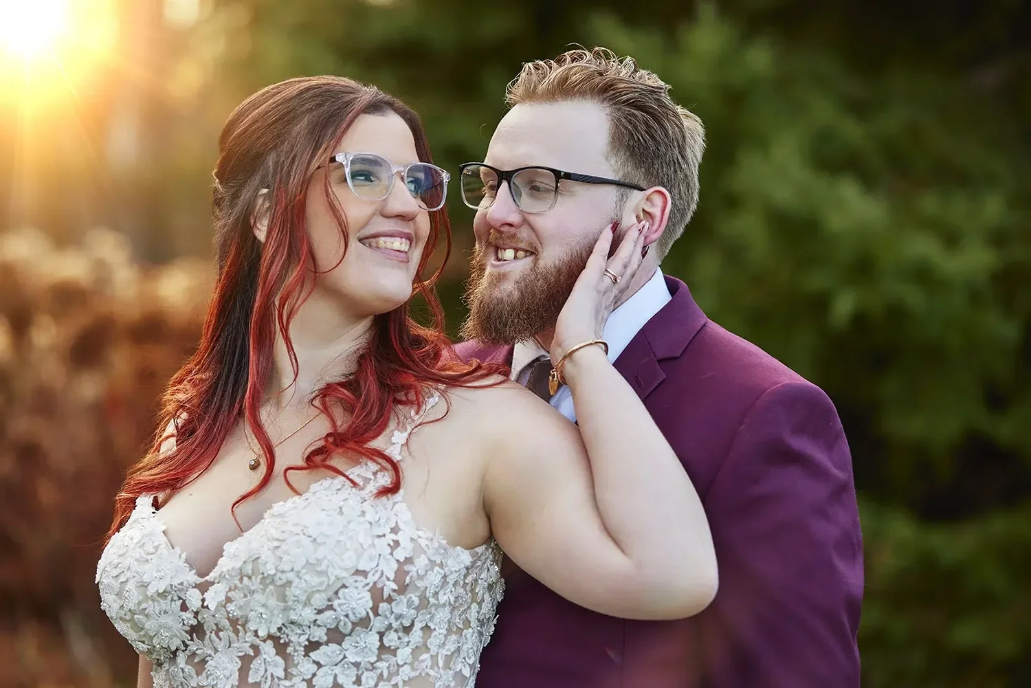 A waiste-up portrait of a bride and groom with trees and late-day sunlight in the background.