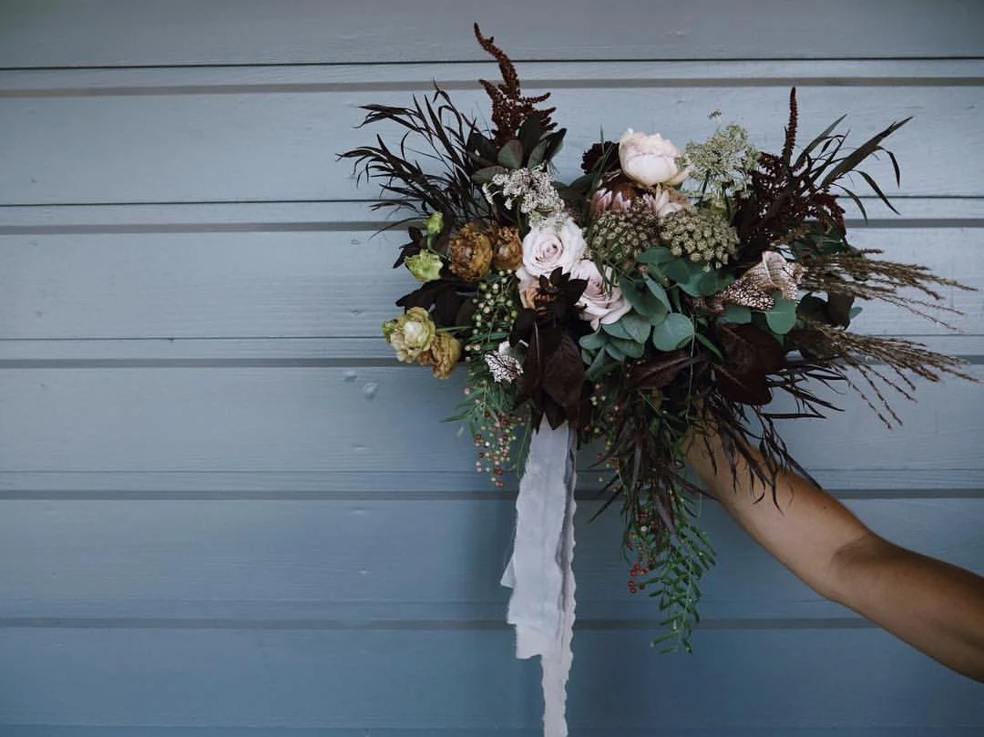 A person holding a bouquet of flowers against a light blue wooden wall.
