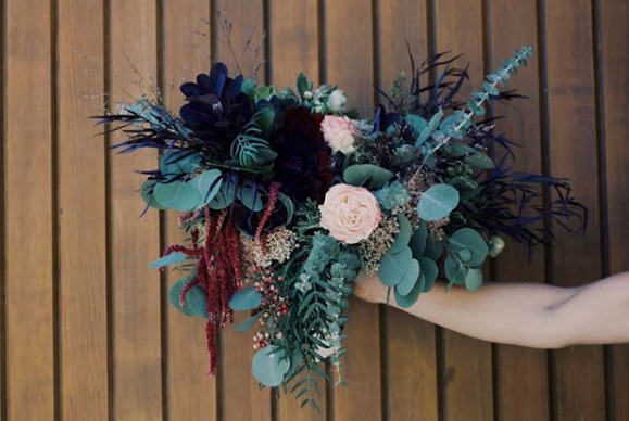 Person holding a large bouquet of flowers against a wooden fence background.