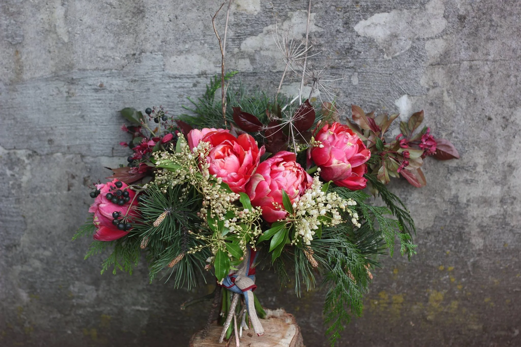 A bouquet of pink peonies, white flowers, and greenery tied with a ribbon, placed against a gray textured background.