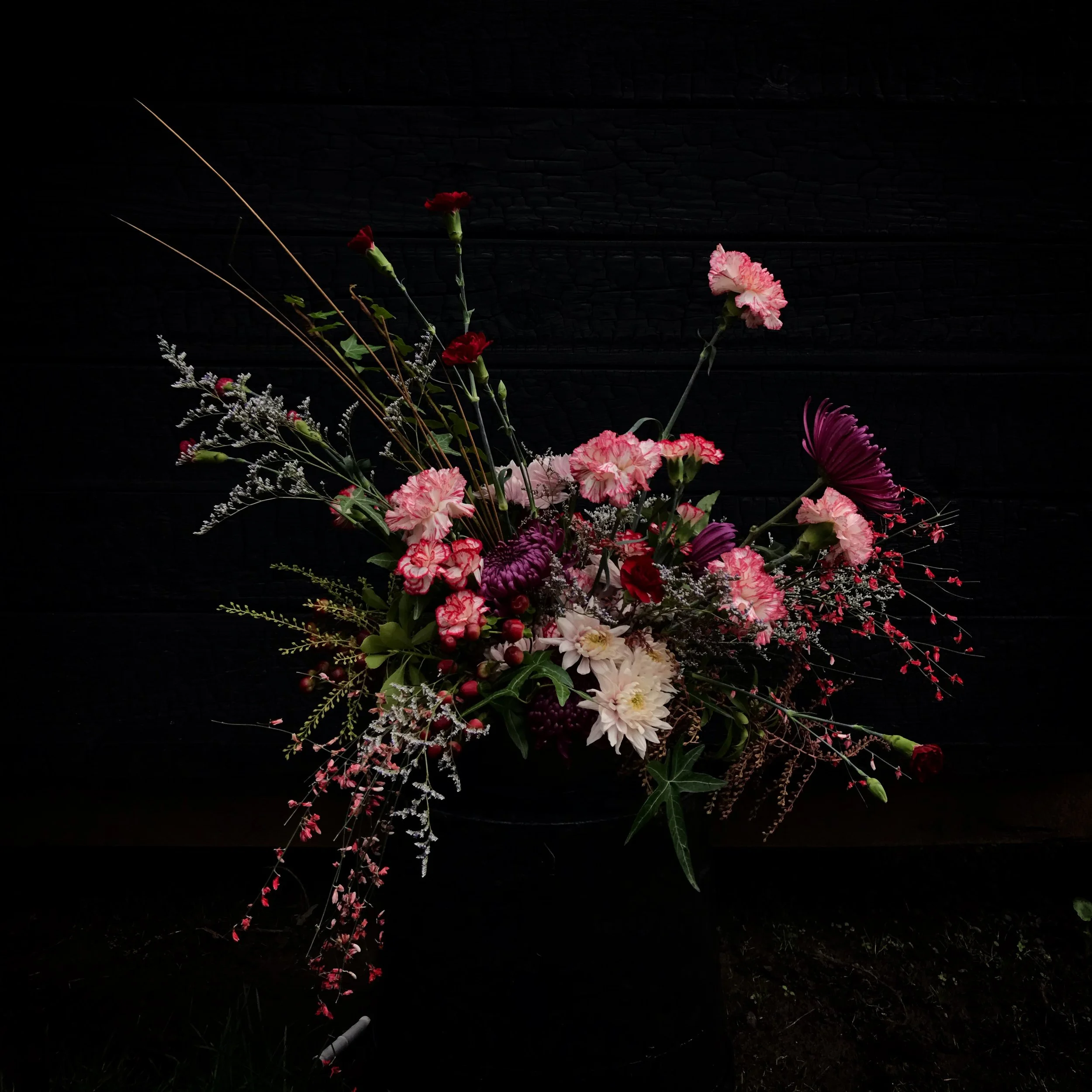 A colorful floral arrangement with pink, white, red, and purple flowers against a dark background.
