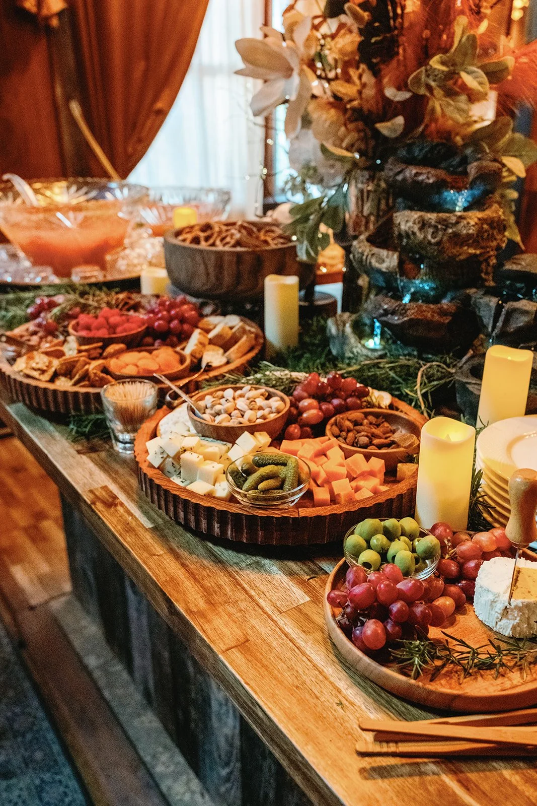 A festive table with a variety of cheeses, grapes, nuts, pickles, and crackers, decorated with candles and flowers.
