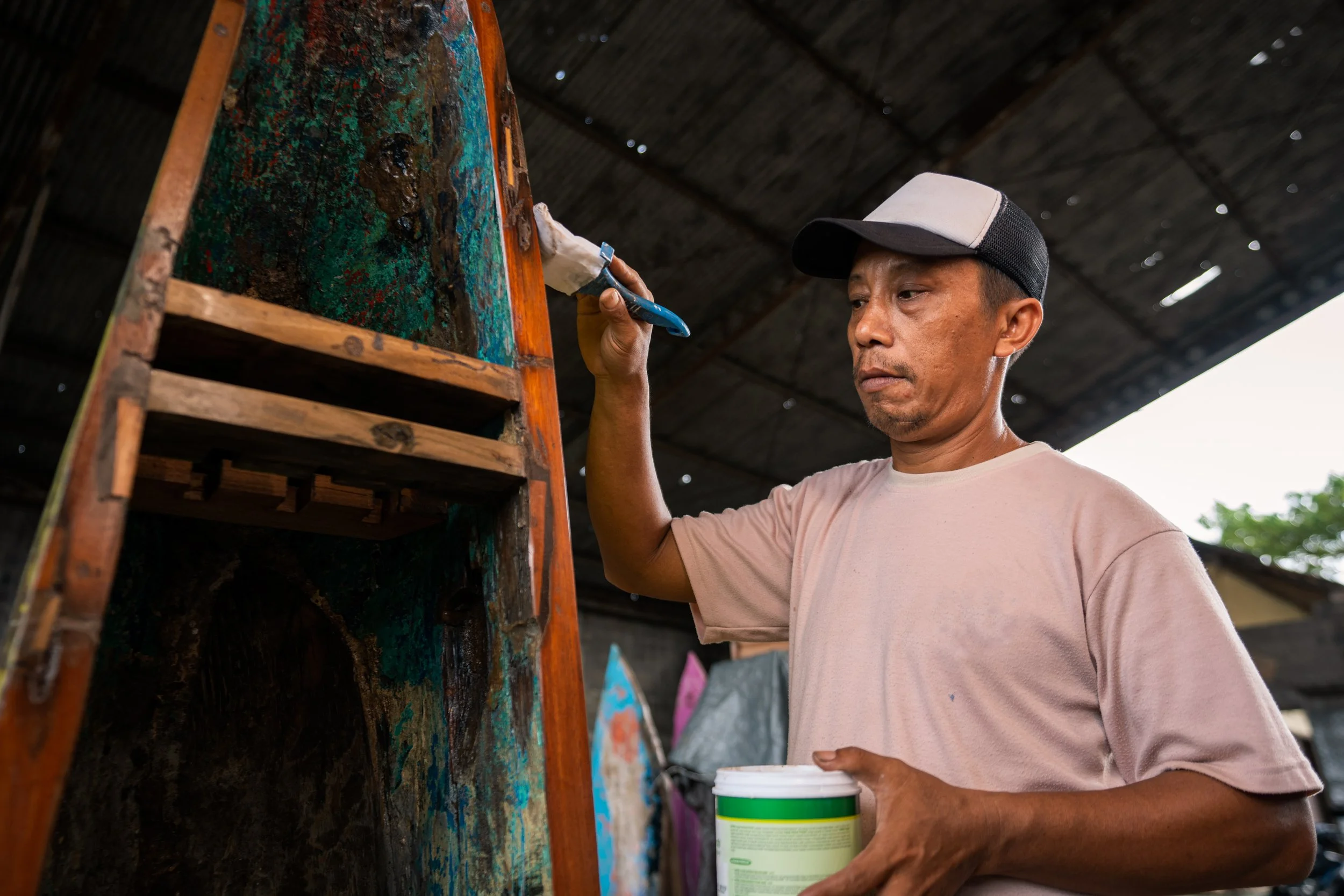 Craftsman meticulously restoring the vibrant paint on a reclaimed wooden boat at PAAT Designs workshop.