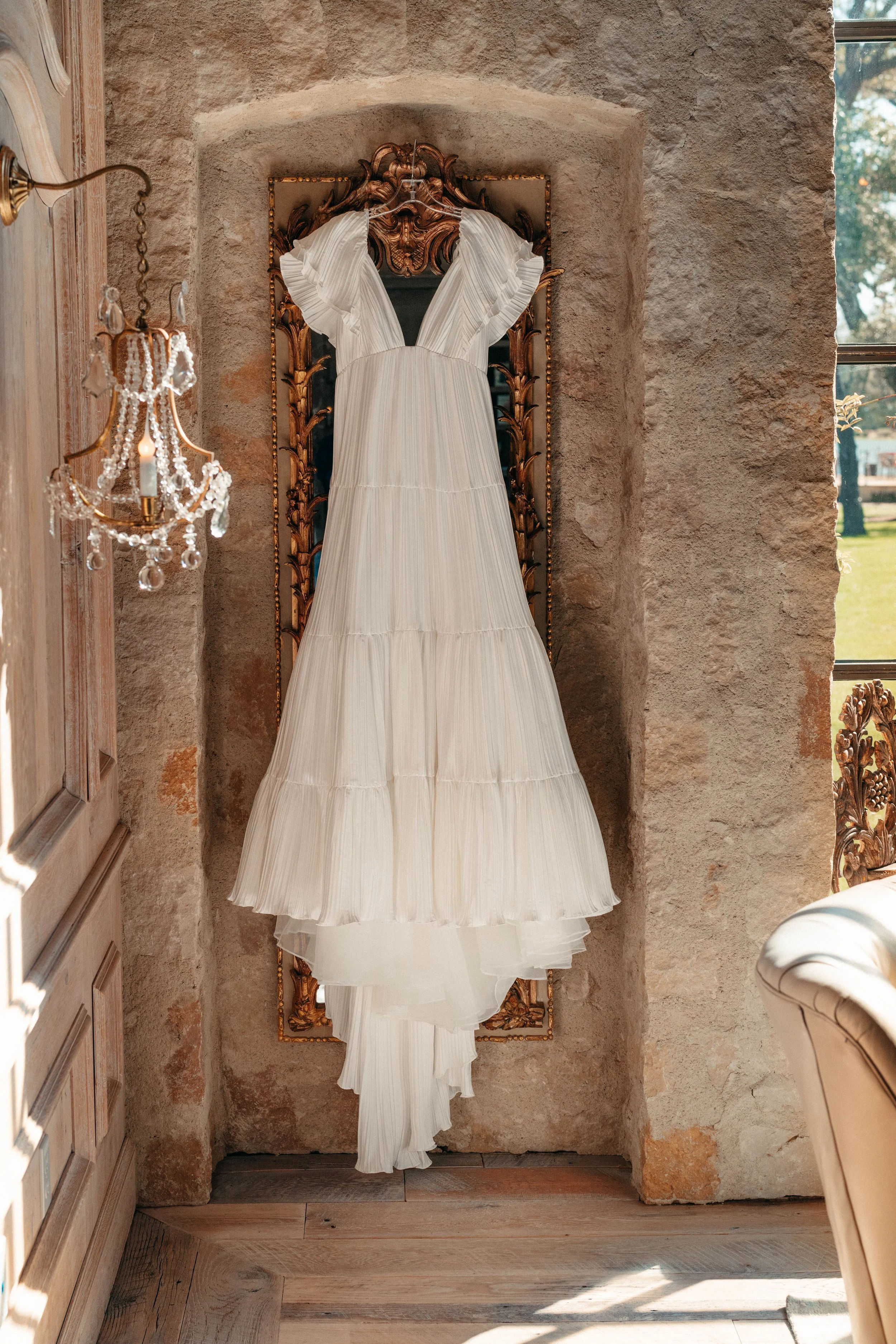 Pleated wedding gown hanging by a window before the ceremony | authentic documentary wedding photography.