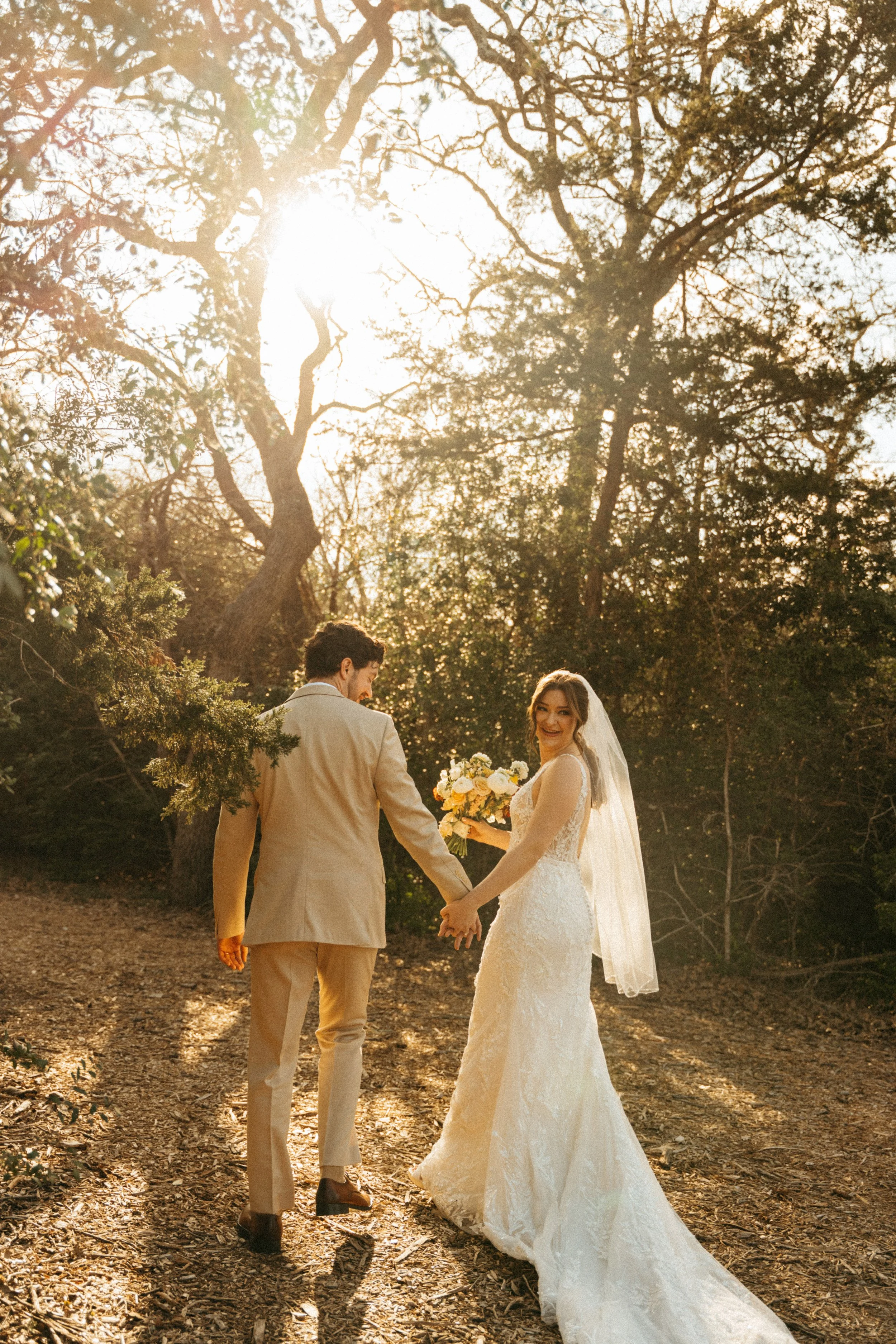 Bride and groom walking hand in hand down oak-lined path at The Grand Lady Manor TX