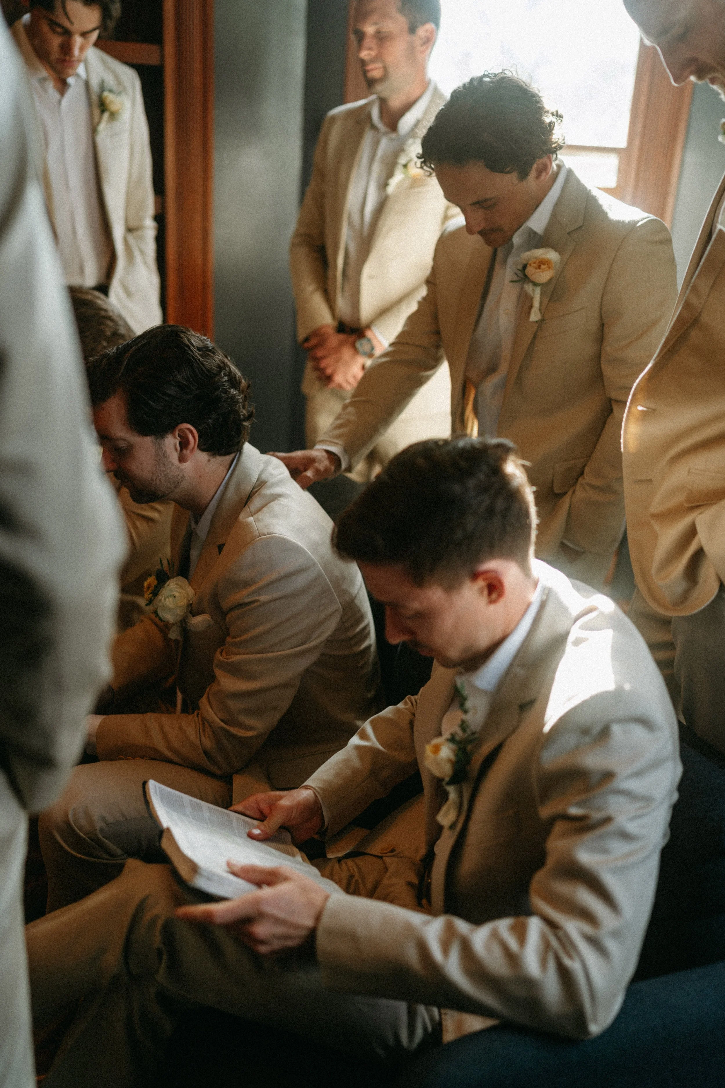 documentary style wedding photography candid of the groom being prayed over by groomsmen in the old money library at The Grand Lady in manor tx just outside of austin