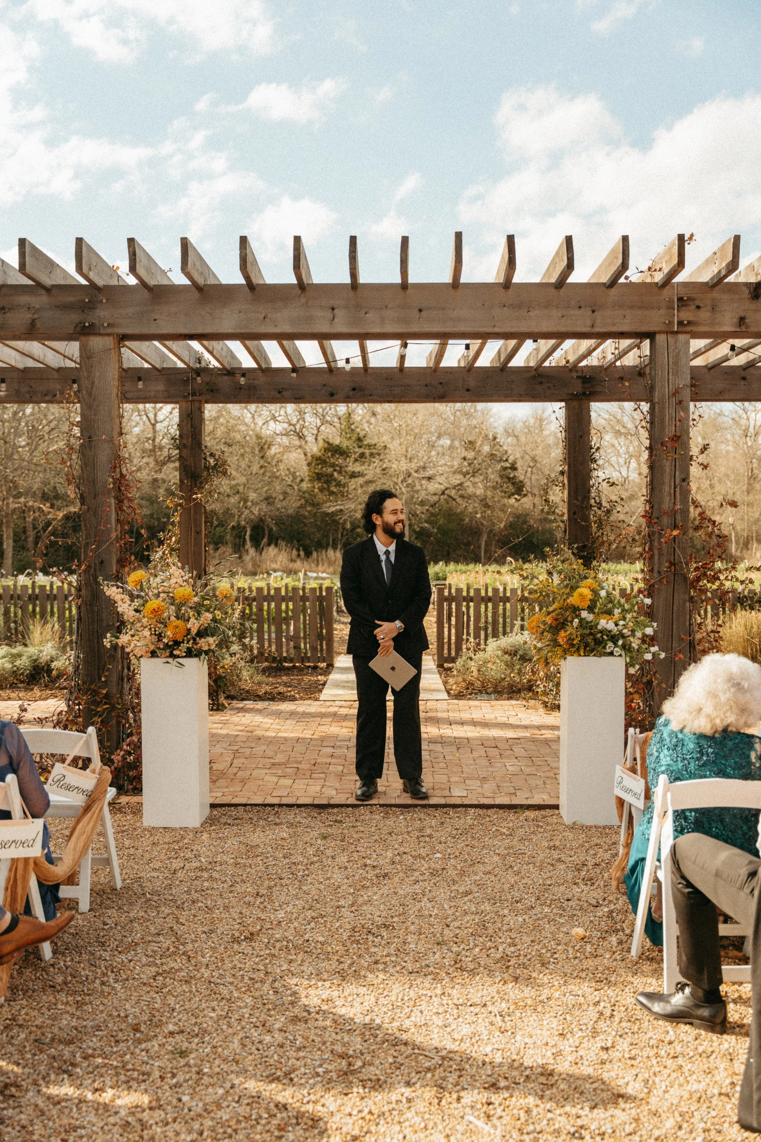 Officiant waits for couple at Grand Lady Florals flower garden during an Austin wedding ceremony at The Grand Lady