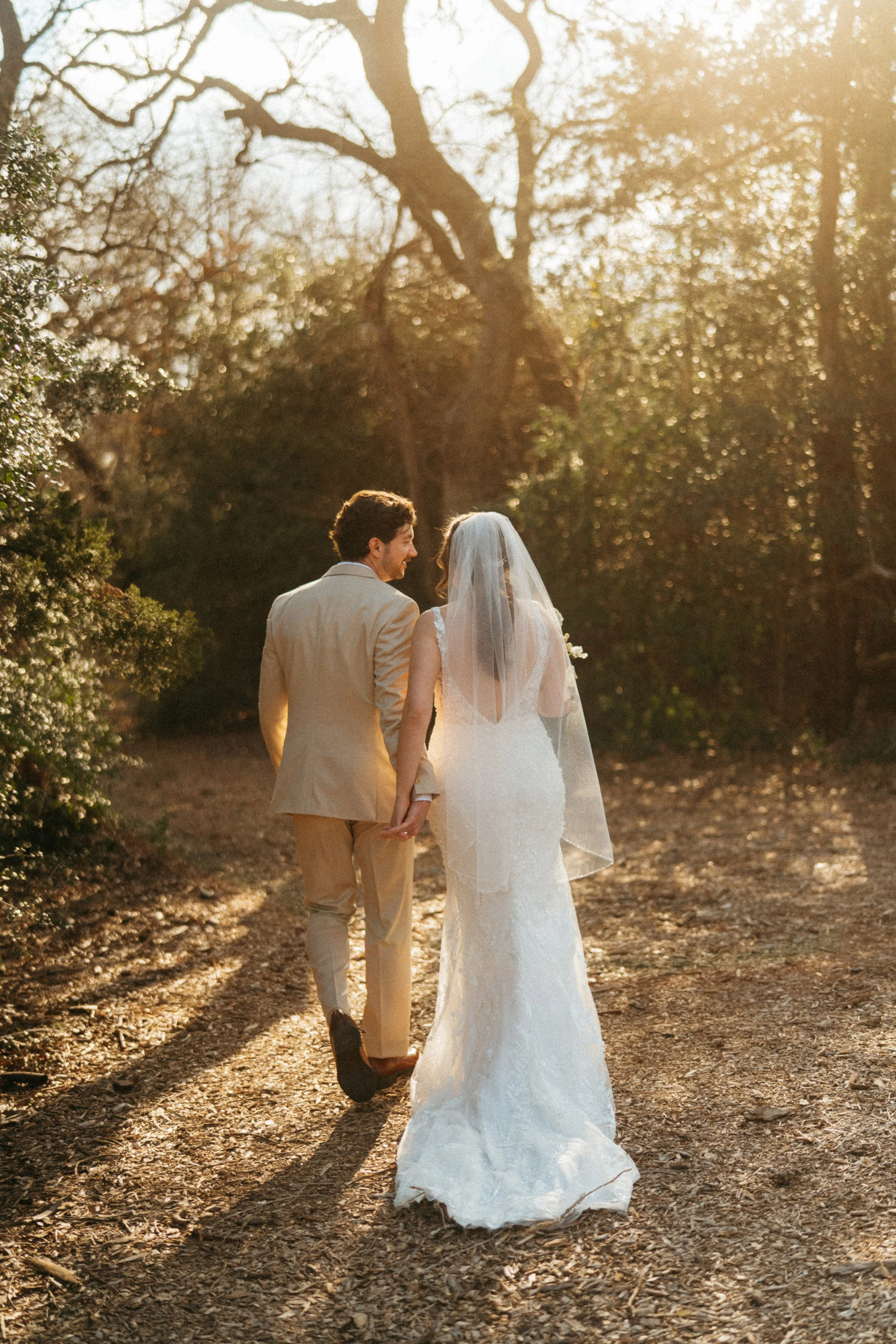Bride and groom walking hand in hand down oak-lined path at The Grand Lady Manor TX
