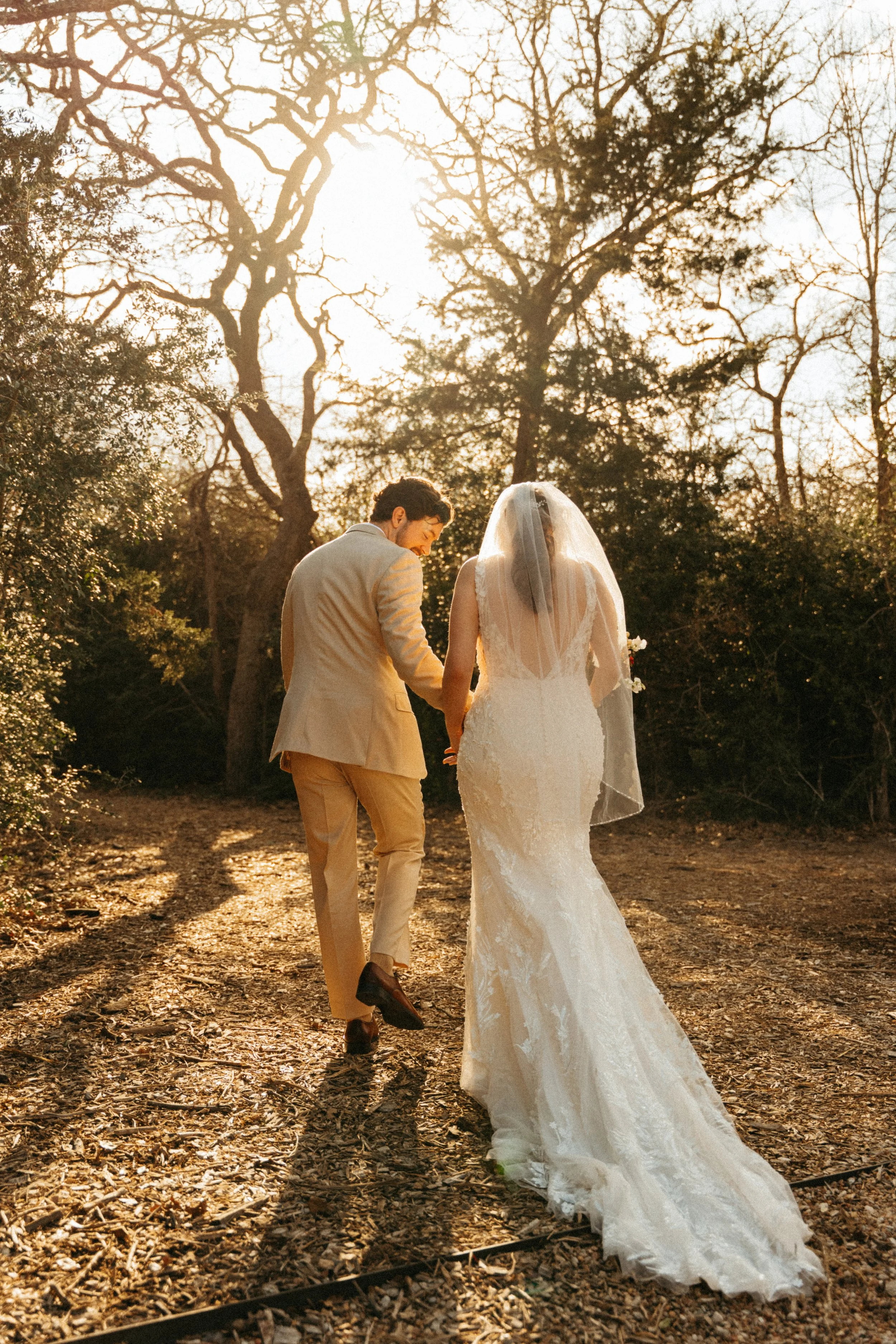 Bride and groom walking hand in hand down oak-lined path at The Grand Lady Manor TX