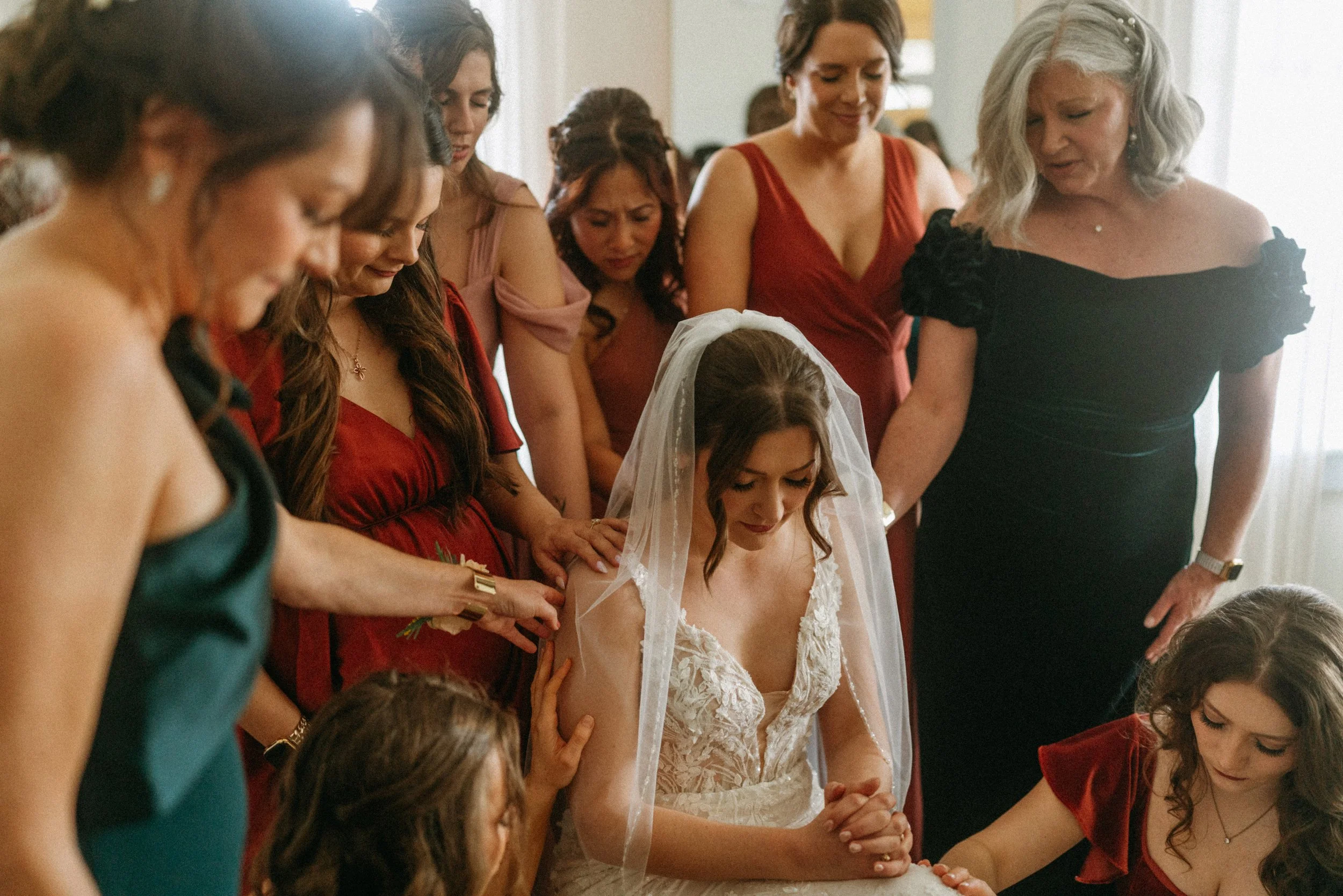 documentary style wedding photography candid of the bride being prayed over by her bridesmaids in the light airy bridal suite at The Grand Lady in manor tx just outside of austin