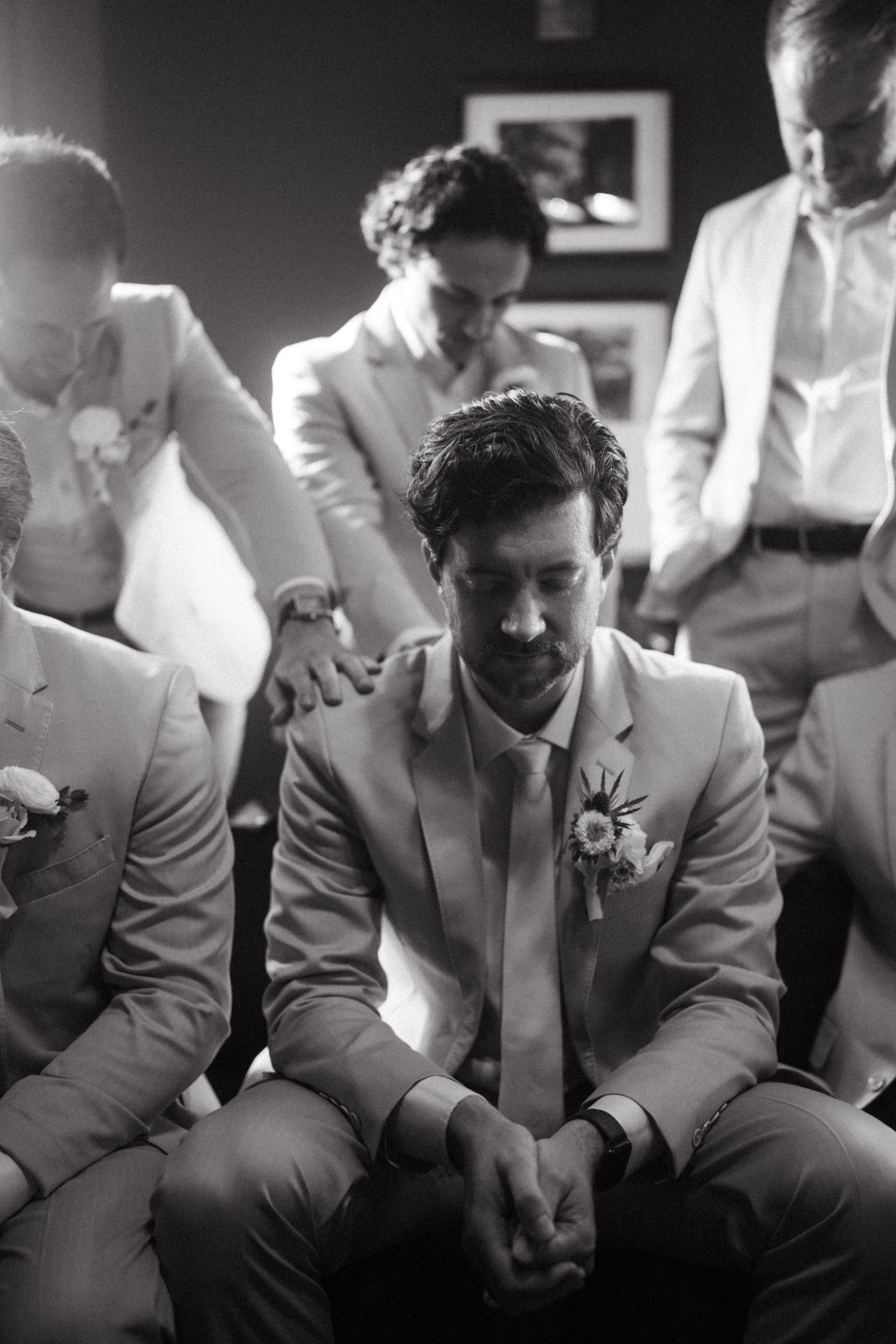 documentary style wedding photography candid of the groom being prayed over by groomsmen in the old money library at The Grand Lady in manor tx just outside of austin