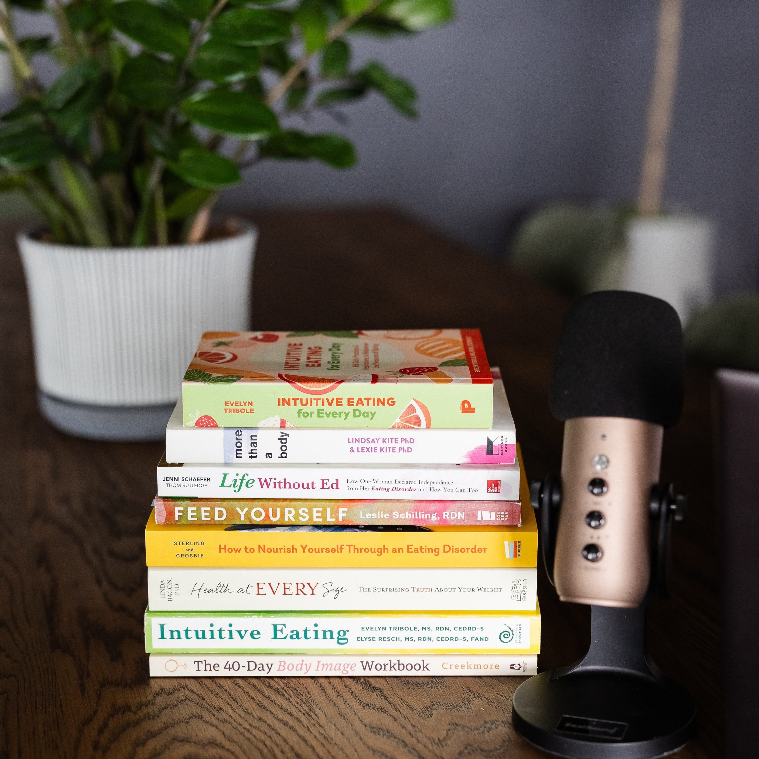 The Truth Based Nutrition podcast microphone and stack of books representing Maddox Nutrition's nutrition and mental health philosophies including Intuitive Eating, Health at Every Size, and Feed Yourself