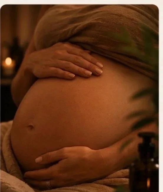 Close-up of a pregnant woman's belly being gently held by her hands in a dimly lit room.