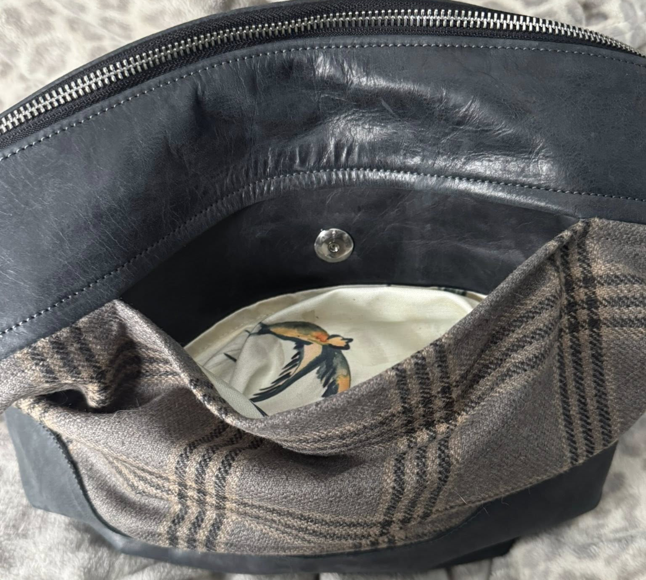 Inside of a black leather bag with a plaid fabric exterior, containing a piece of fabric with a bird print.