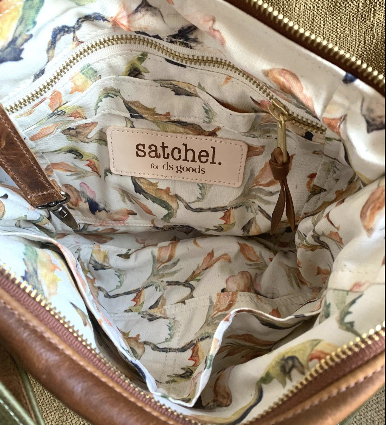 Inside of a bag with floral lining, showing a label that reads 'satchel for ds goods' and a zipped pocket.