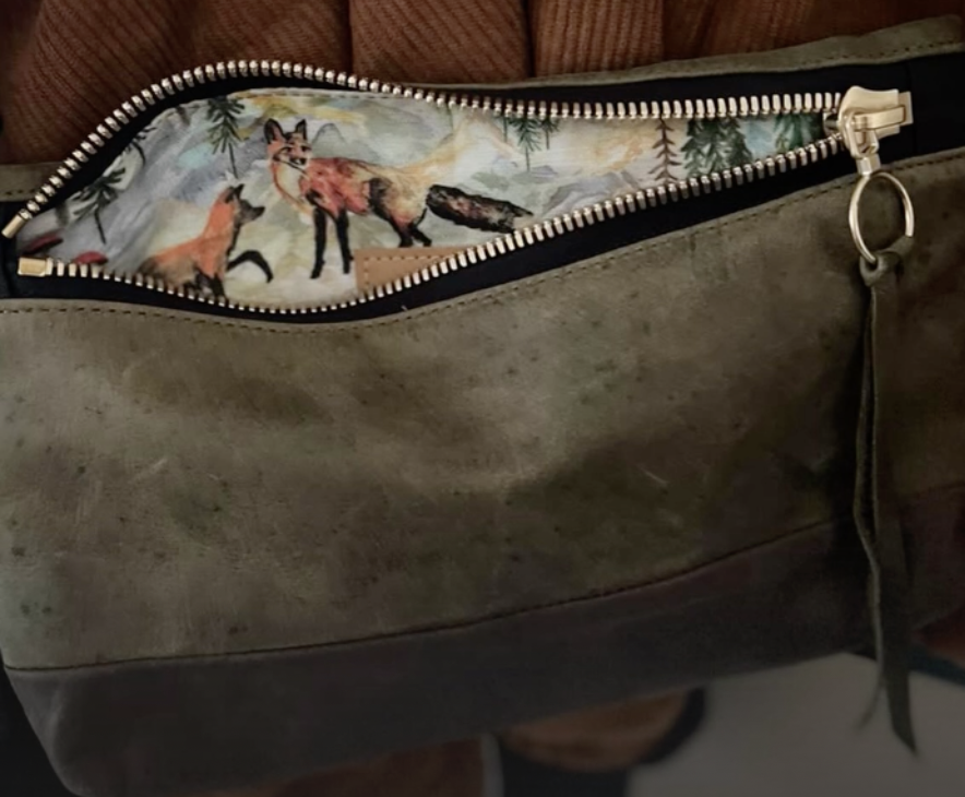 Brown purse with a zipper pocket partly open, showing a fabric lining with fox and forest scene illustrations.
