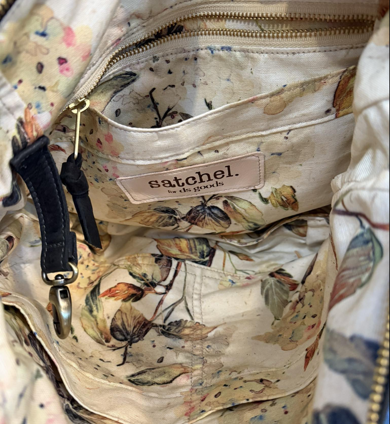 Inside of a floral patterned bag with a brand label that reads 'satchel. for ds goods' and a zippered pocket.