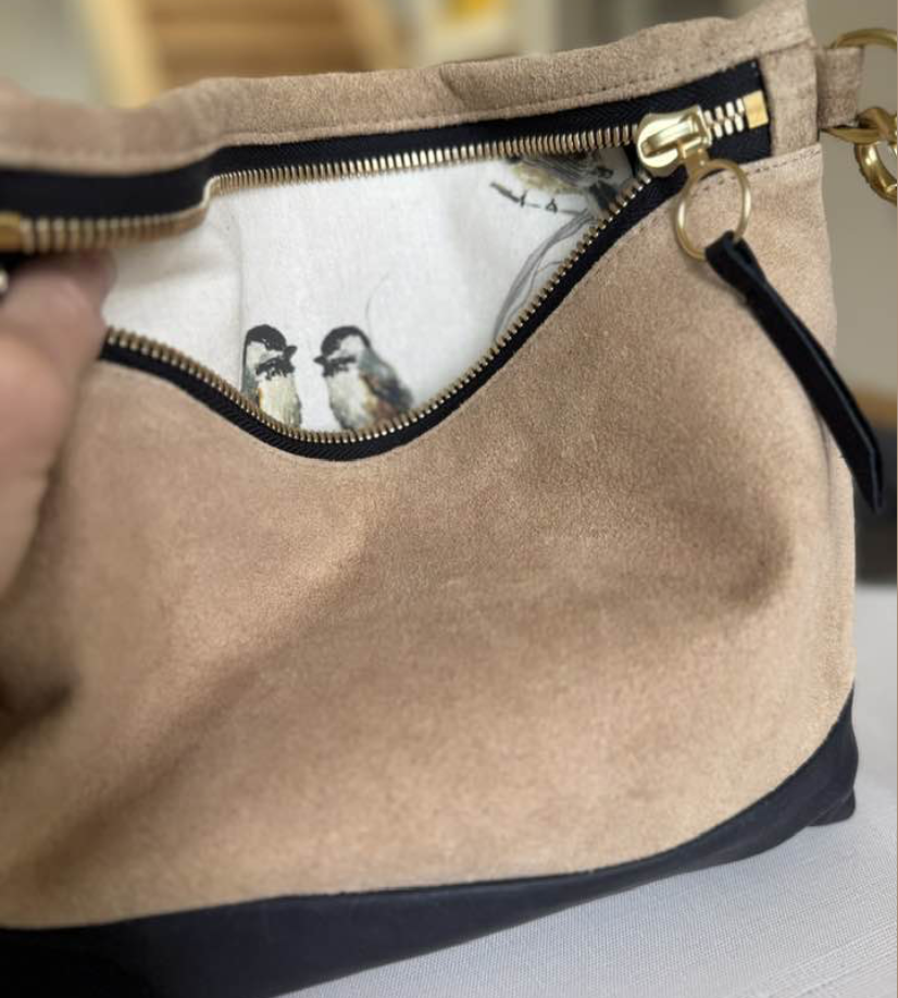 A tan purse with a partially unzipped front pocket revealing two small birds inside.
