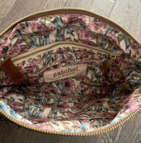 The inside of a floral-patterned fabric bag with a zipper pocket and a label that reads 'Satchel'.