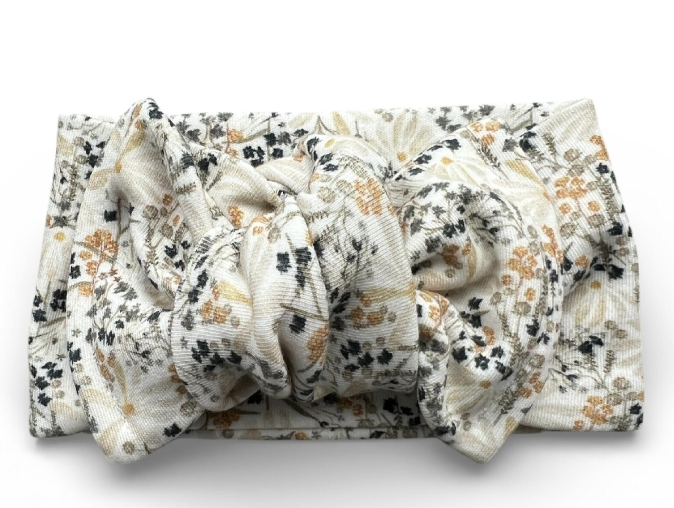 A fabric headband with a floral pattern featuring black, orange, and beige flowers, placed on a folded piece of matching fabric on a white background.