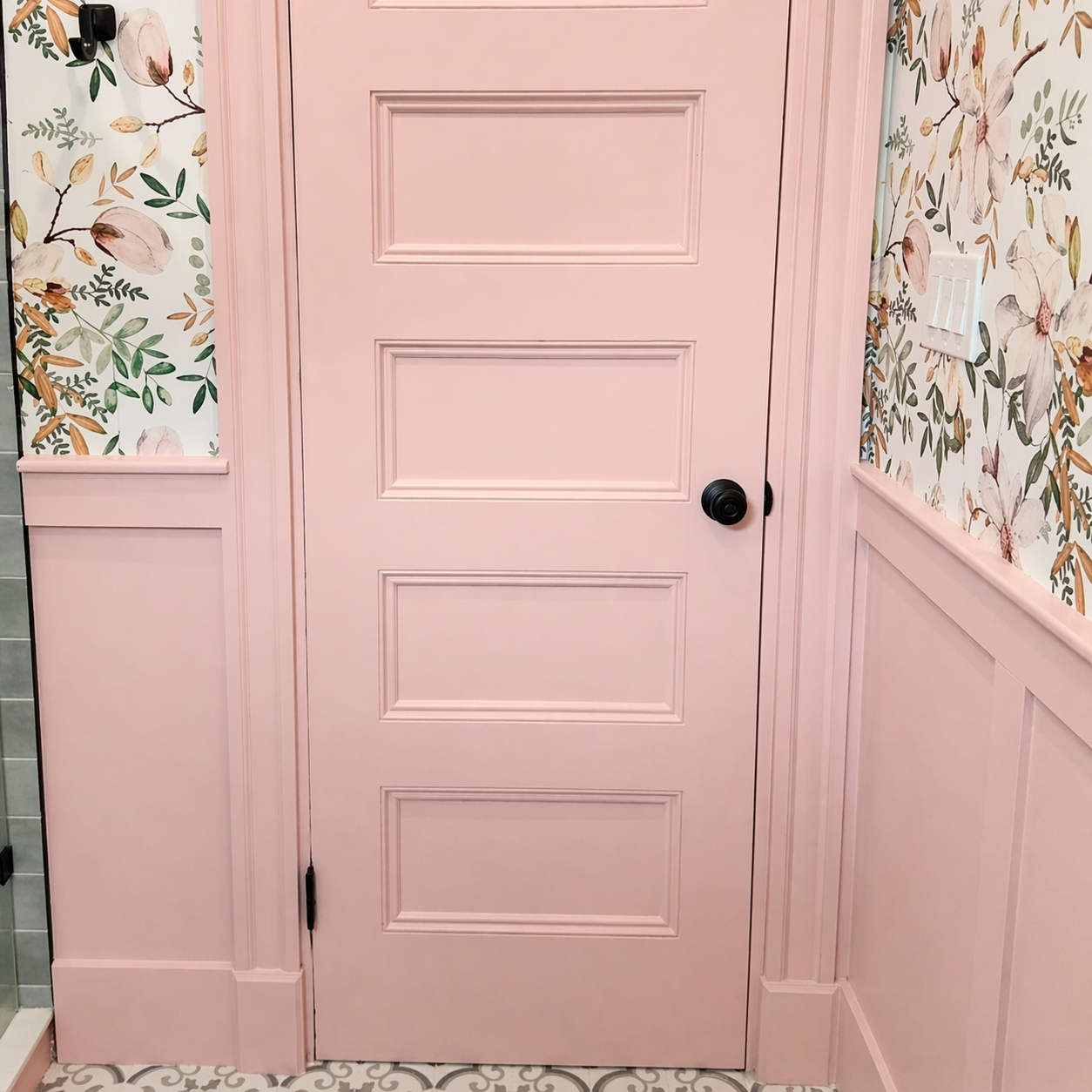 Pink door with black doorknob, floral wallpaper on the walls, and a pink painted panel on the lower wall. Text overlay reads 'The Carpenter Chick Boston.'