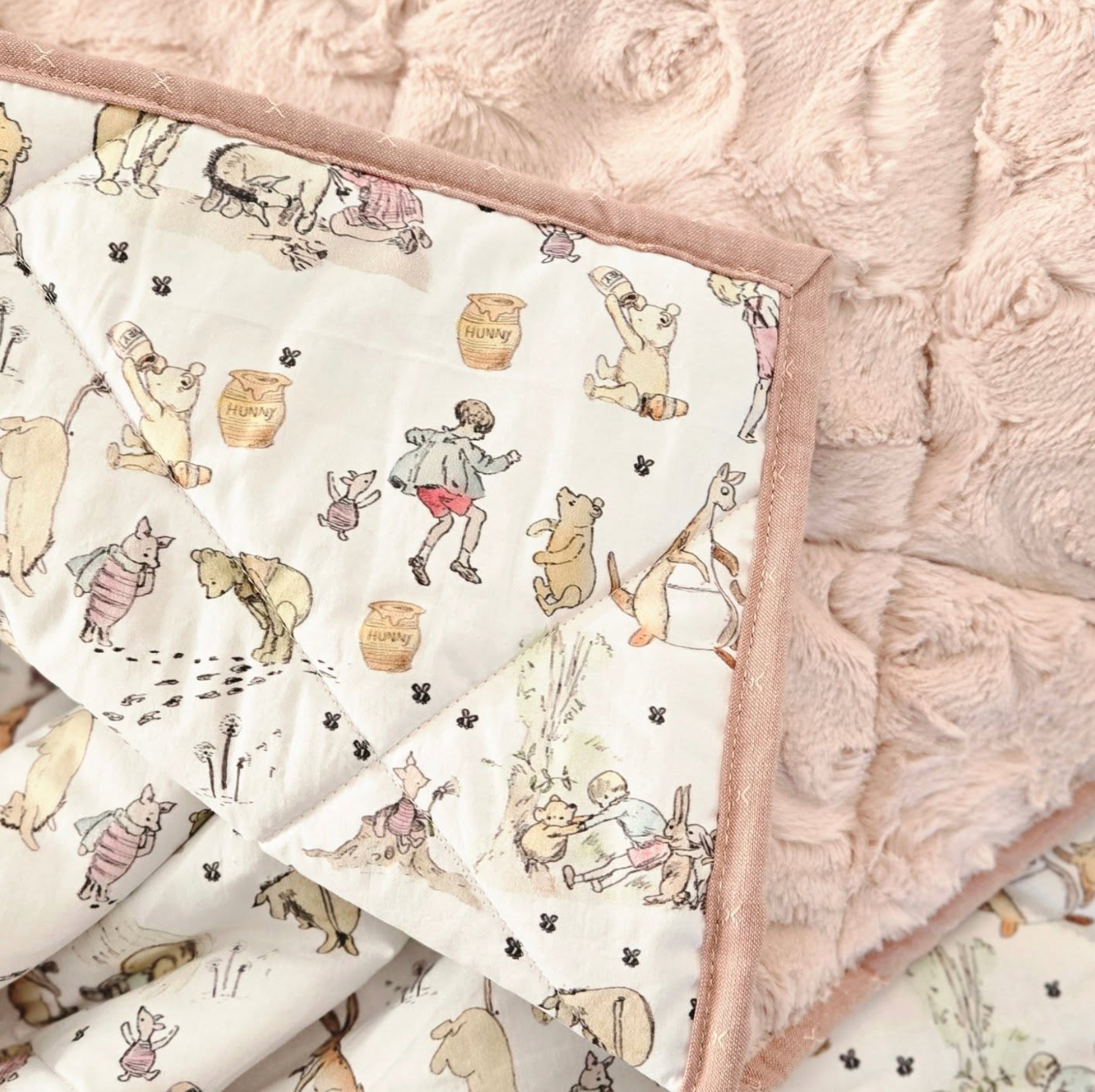 Close-up of a children's quilt with illustrations of animals and children, laid over a fluffy pink blanket.