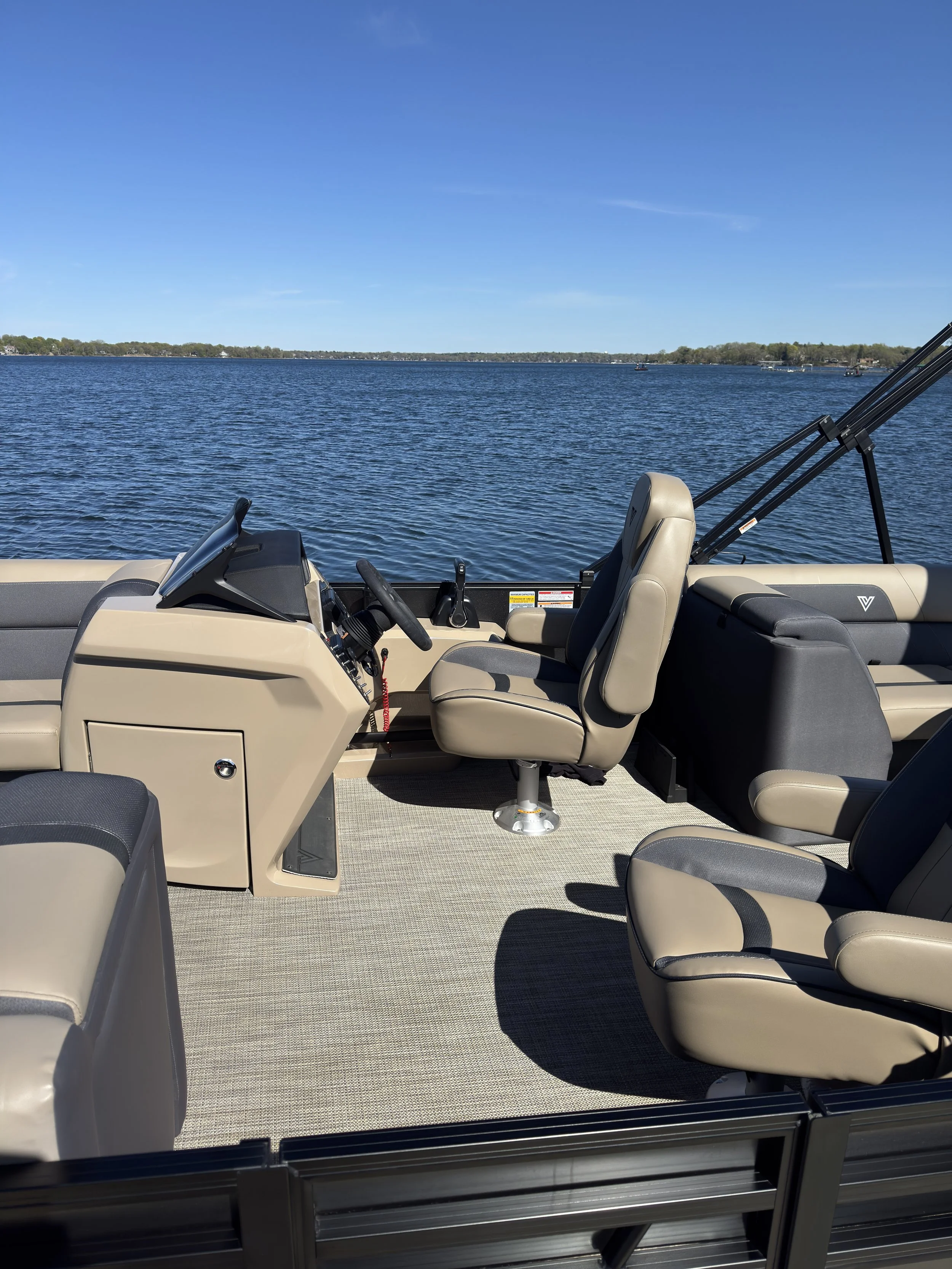 View from inside a boat with beige and black seats on a body of water, with a distant shoreline and clear blue sky in the background.