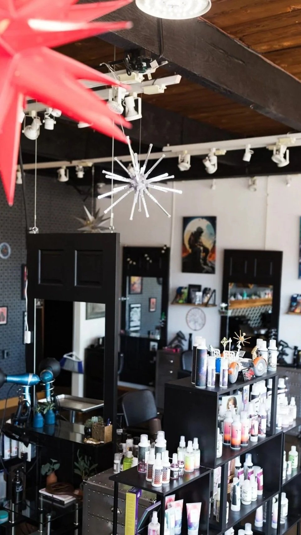 Interior of a salon with shelves holding hair or skincare products, decorative lighting fixtures hanging from a wooden ceiling, and artwork on the walls.