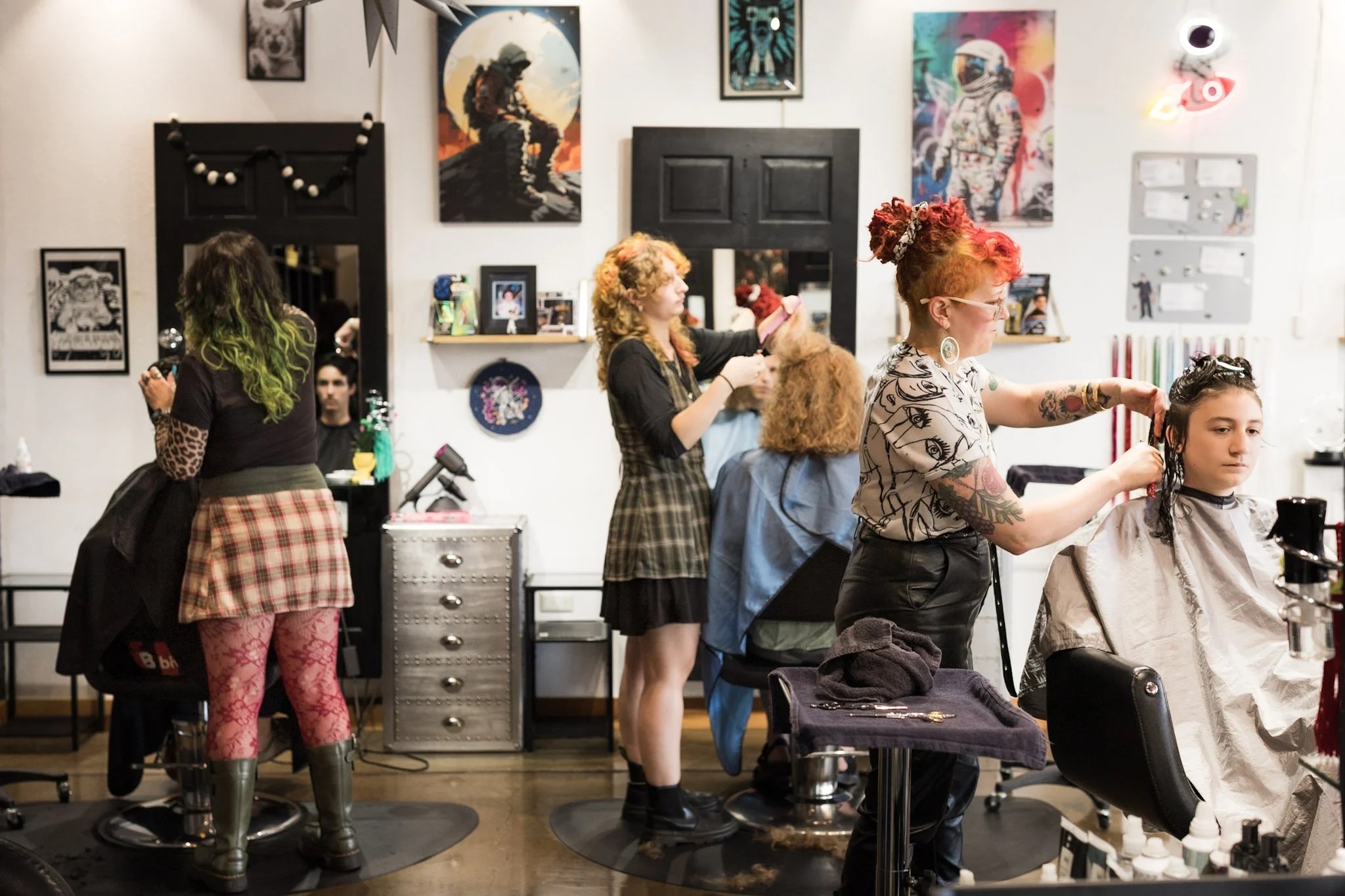 Stylists working on hair in a salon with artwork on the wall, mirrors, and salon chairs.