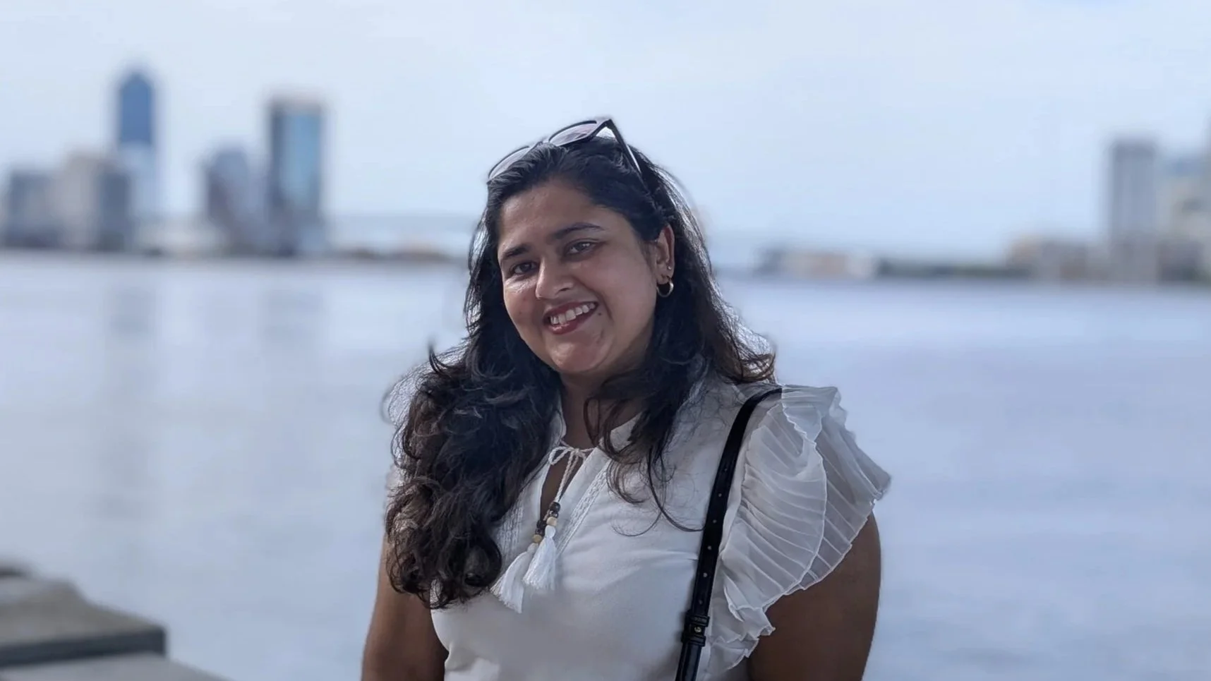 Shonezi the best graphic designer with long dark hair smiling by a body of water with a city skyline in the background.