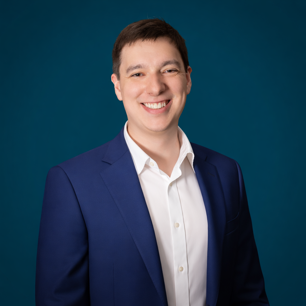 Smiling man in a navy blazer and white shirt posing against a solid dark blue background.