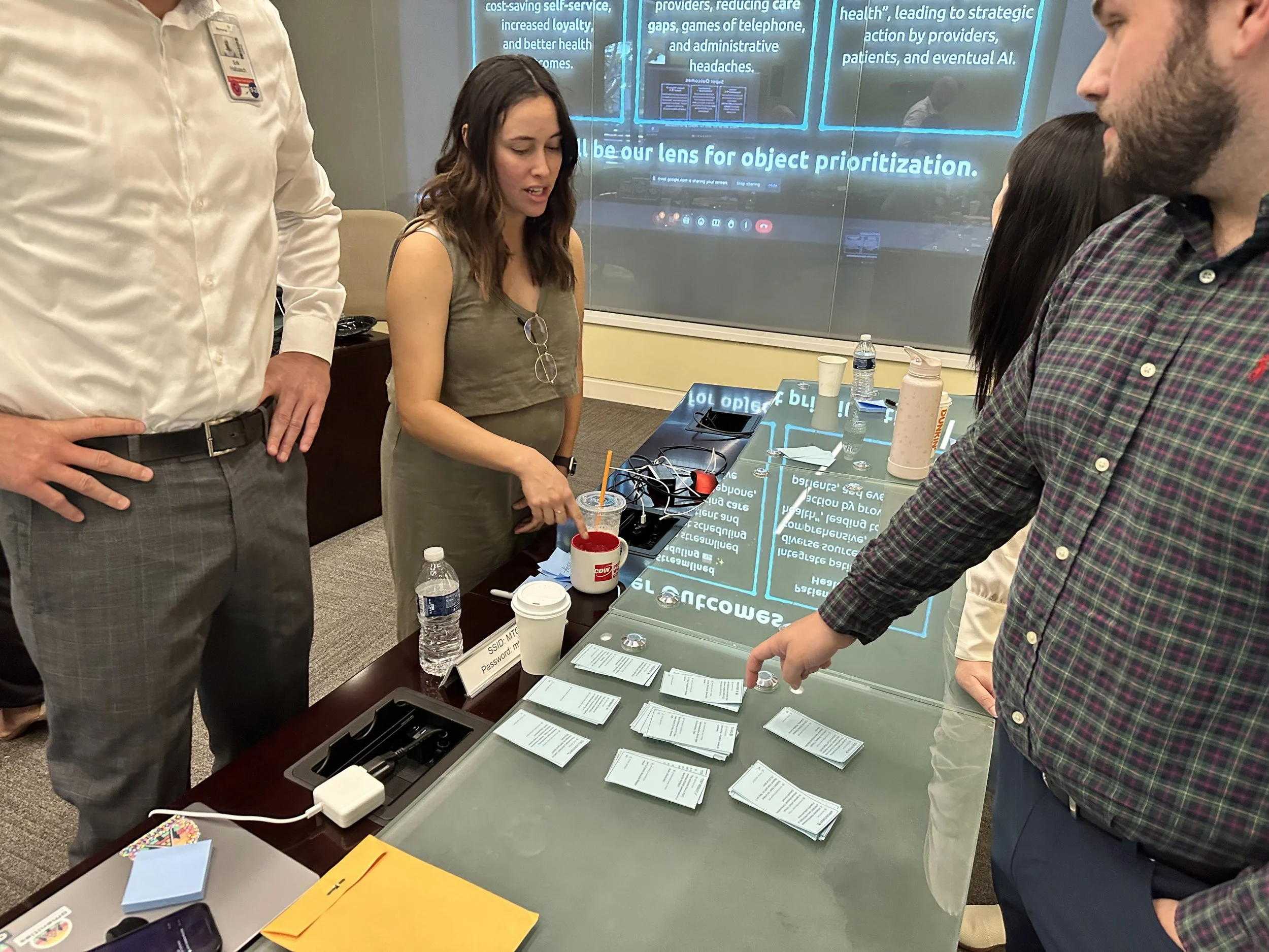 Workshop participants pointing at blue notecards arranged on table during collaborative OOUX session