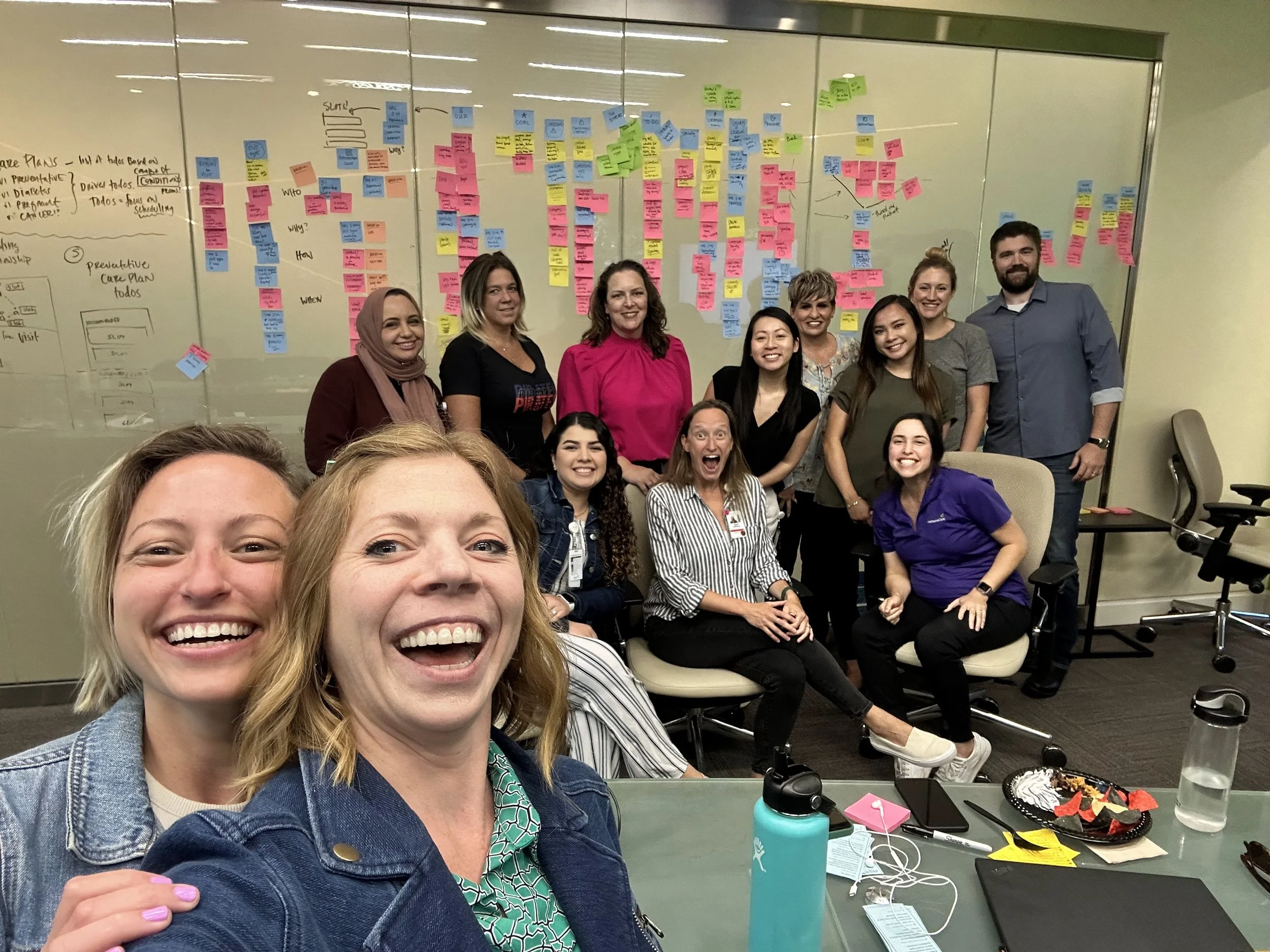 OOUX facilitators Allie Offisher and Sophia Prater with workshop team celebrating completion of three-day ORCA Sprint, colorful sticky notes covering wall behind group