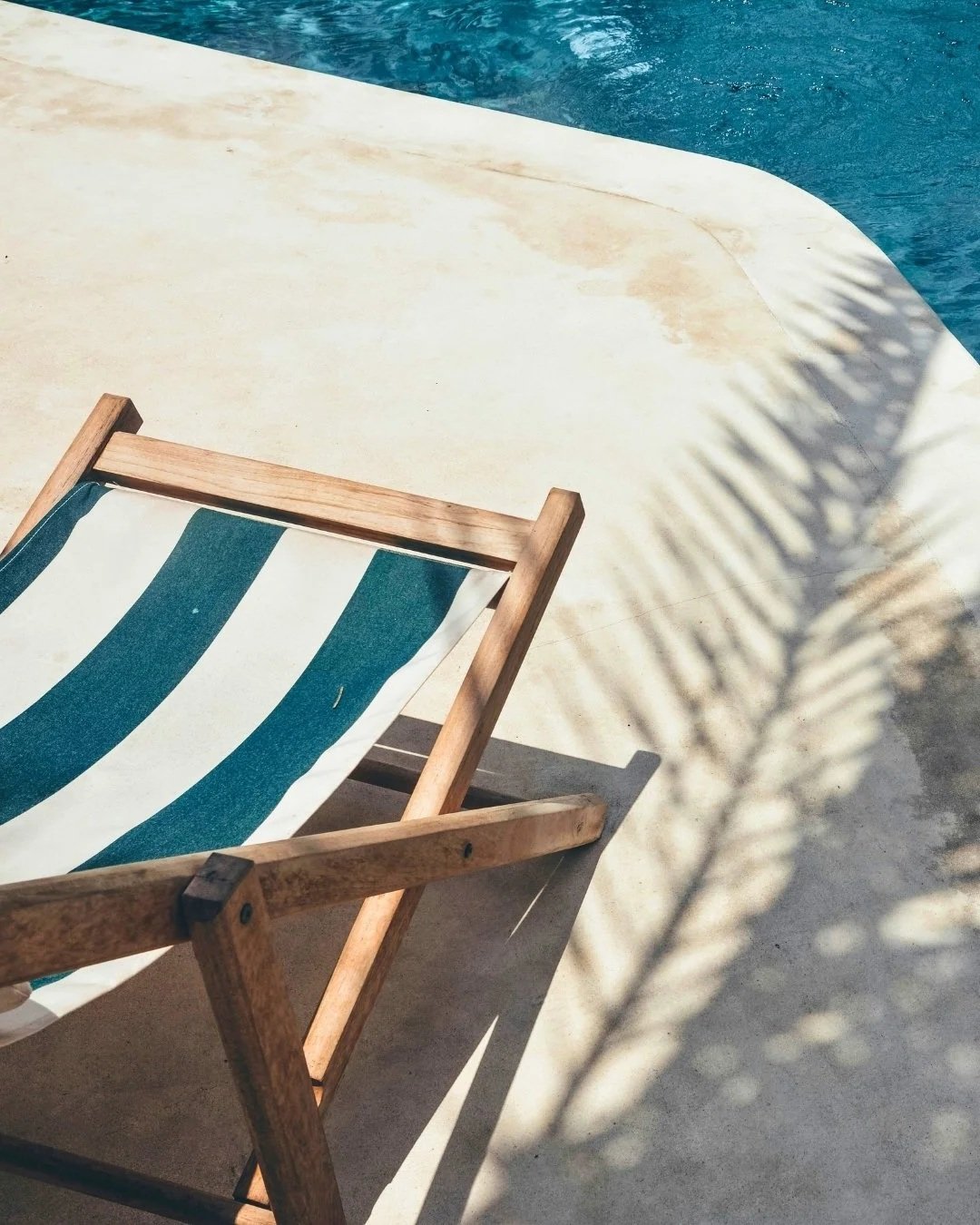 A wooden lounge chair with striped fabric sitting on a rock in Greece.