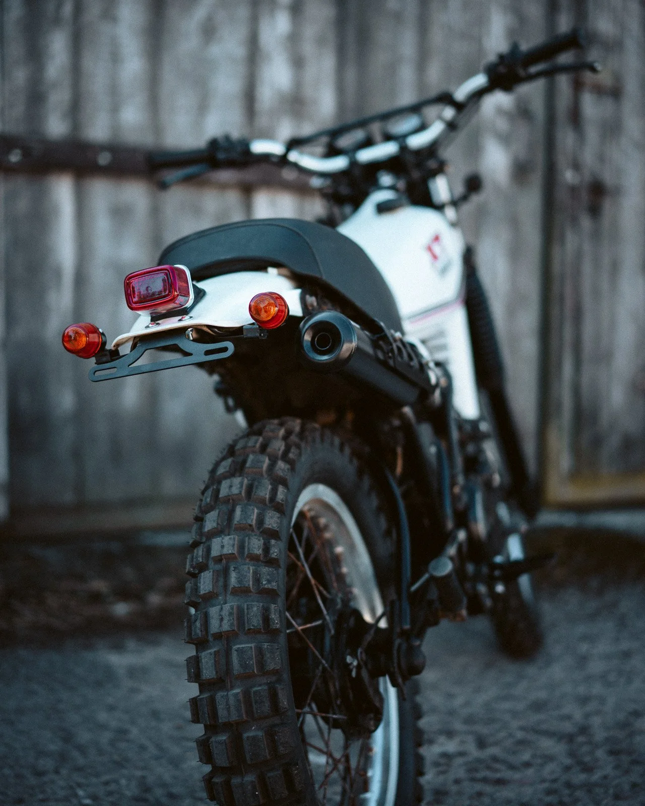 Ein off-road Motorrad mit schwarzem Reifen und weißem Rahmen, geparkt vor einer Holzwand bei Dämmerung.