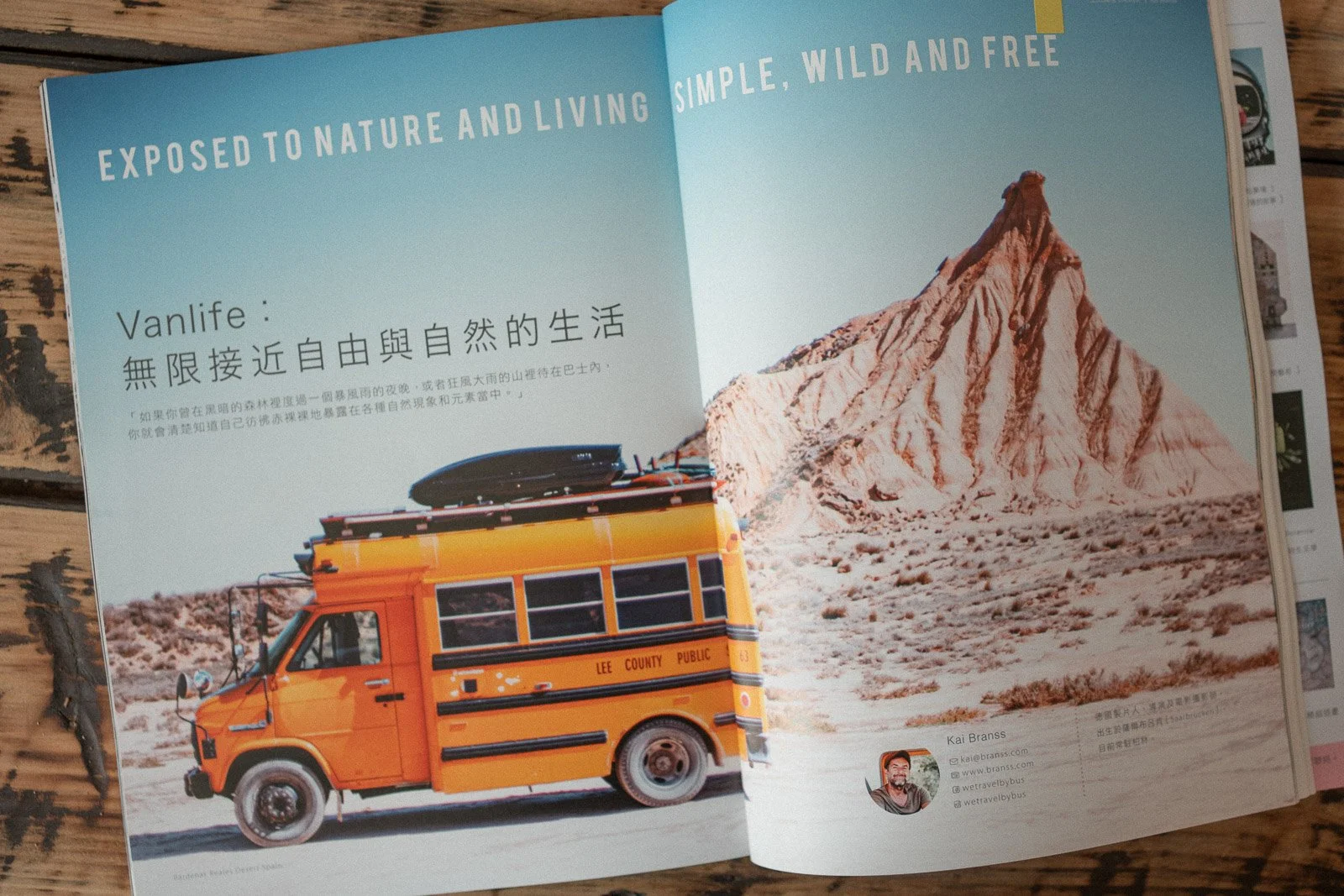 Eine offene Zeitschrift zeigt eine Wüstenlandschaft mit einem großen Berg und einem gelben Bus. Der Text erwähnt Natur, Freiheit und ein einfaches Leben.