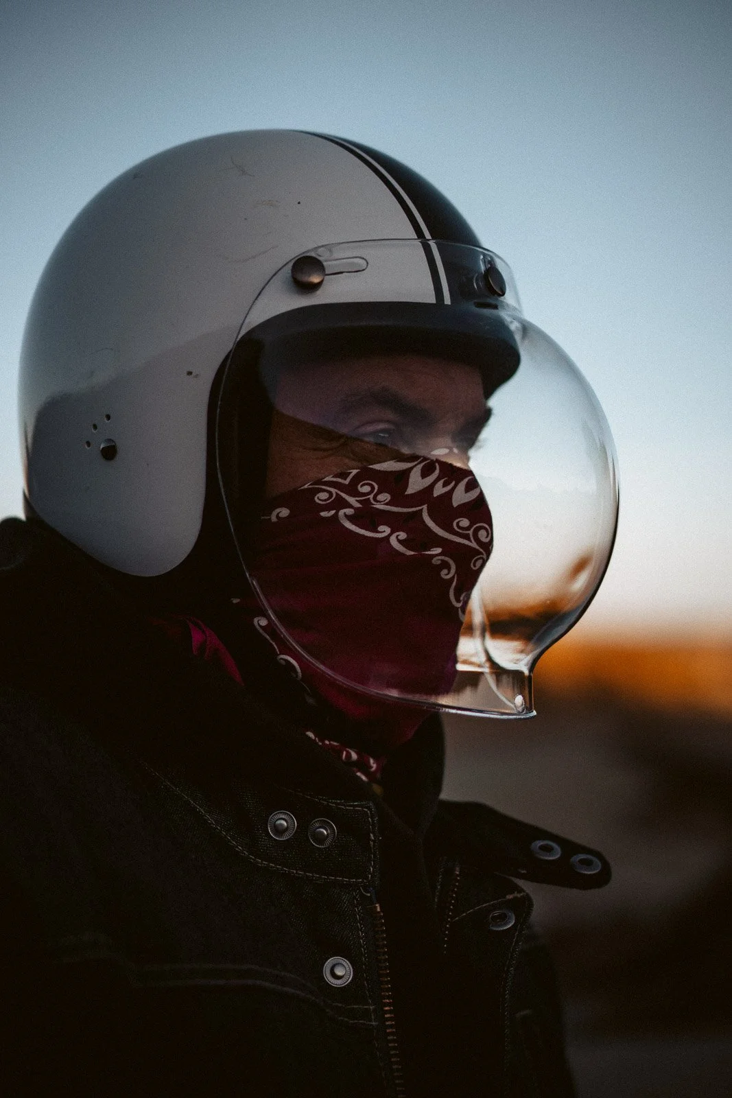 Ein Mann trägt einen weißen Motorradhelm mit UV-Schutzvisier und ein rot-weiß gemustertes Halstuch, während er im Dunkeln unterwegs ist.
