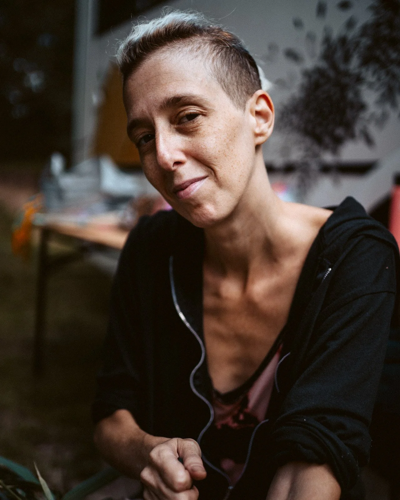 Nahaufnahme einer jungen Frau mit kurzem Haar, die lächelnd in die Kamera schaut, in einer häuslichen Umgebung.