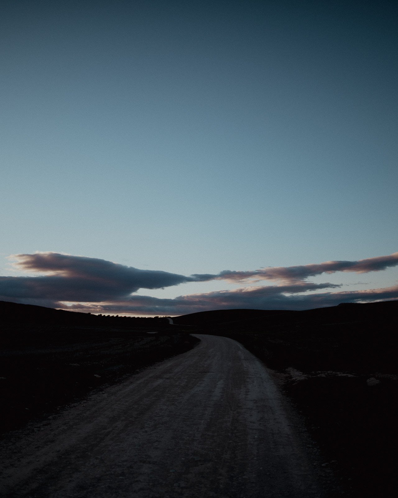 Straße in einer ländlichen Umgebung bei Sonnenuntergang oder Dämmerung, bewölkter Himmel