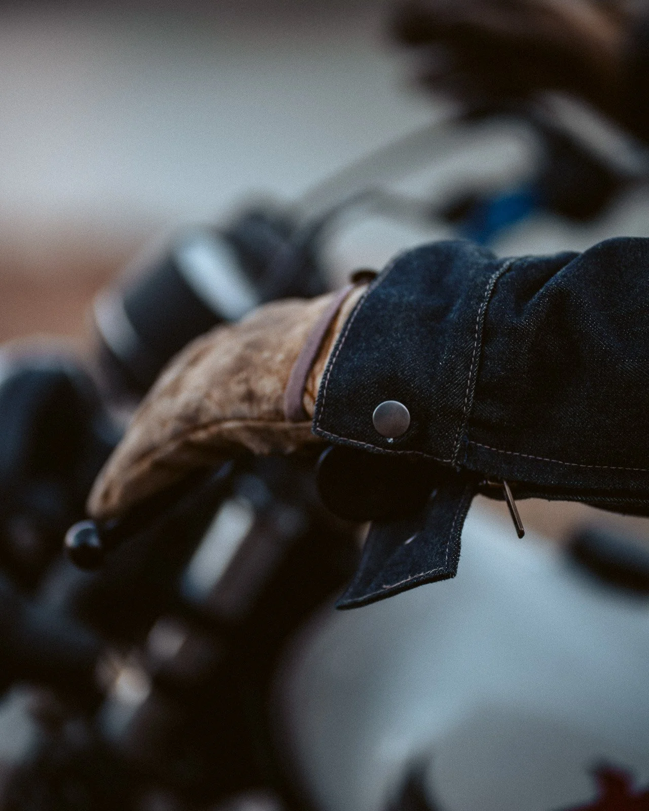 Nahaufnahme eines Motorradlenkers mit schwarzer Jacke und braunem Handschuh, der einen schwarzen Lenker hält.