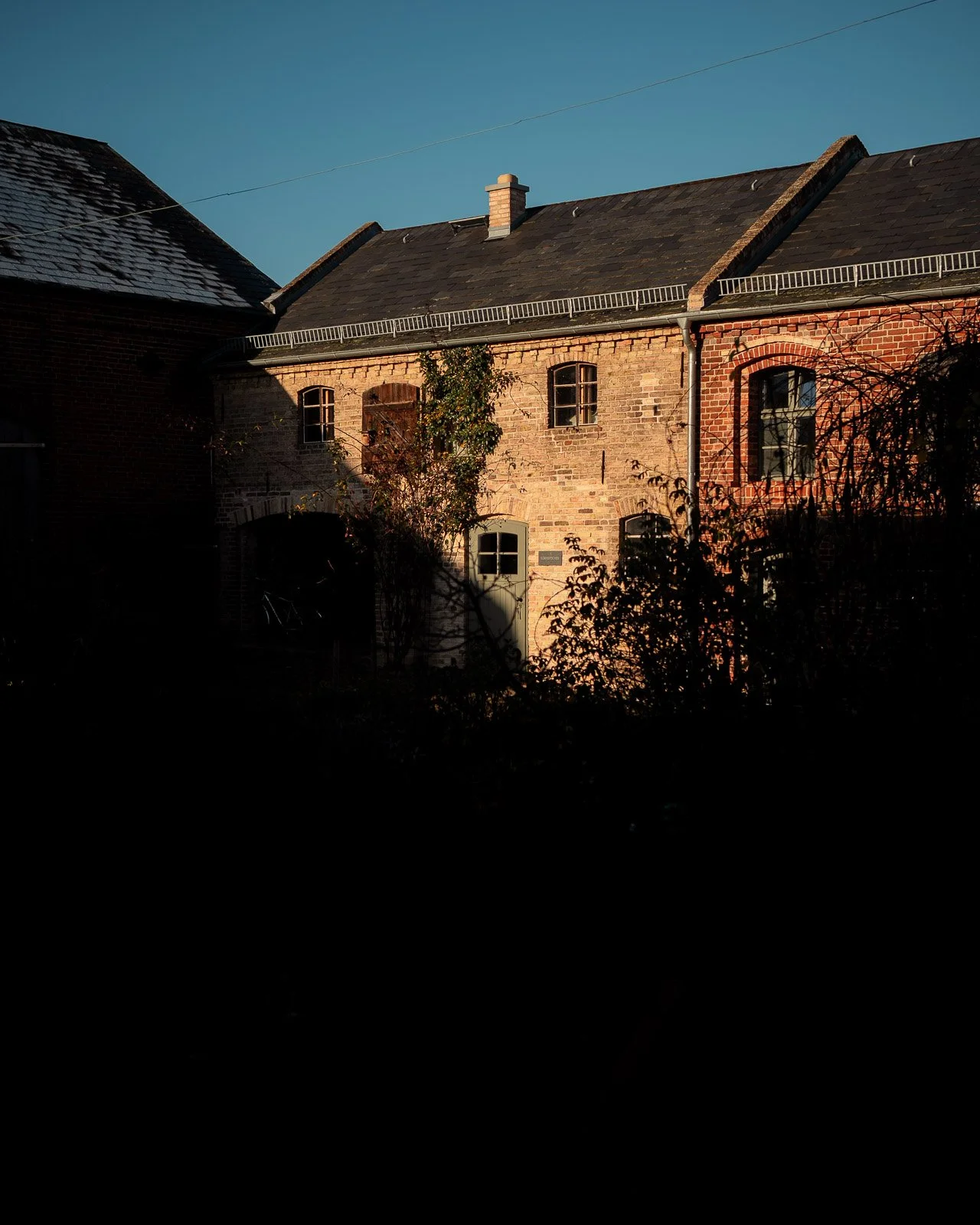 Eine alte Backsteingebäude bei Sonnenuntergang, teilweise im Schatten, mit Bäumen im Vordergrund.