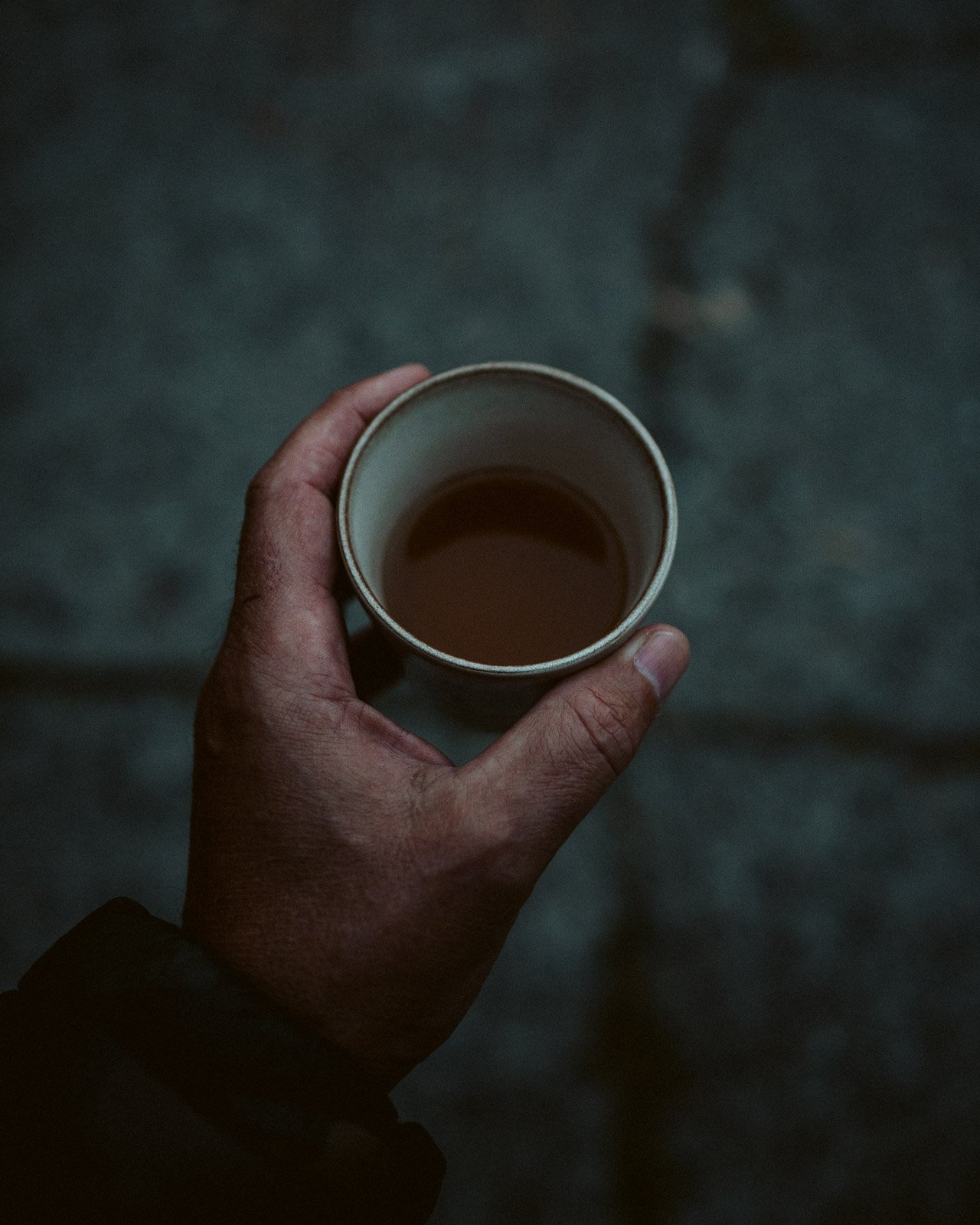 Nahaufnahme einer Hand, die eine Tasse mit heißem Getränk hält, auf dunklem Hintergrund.