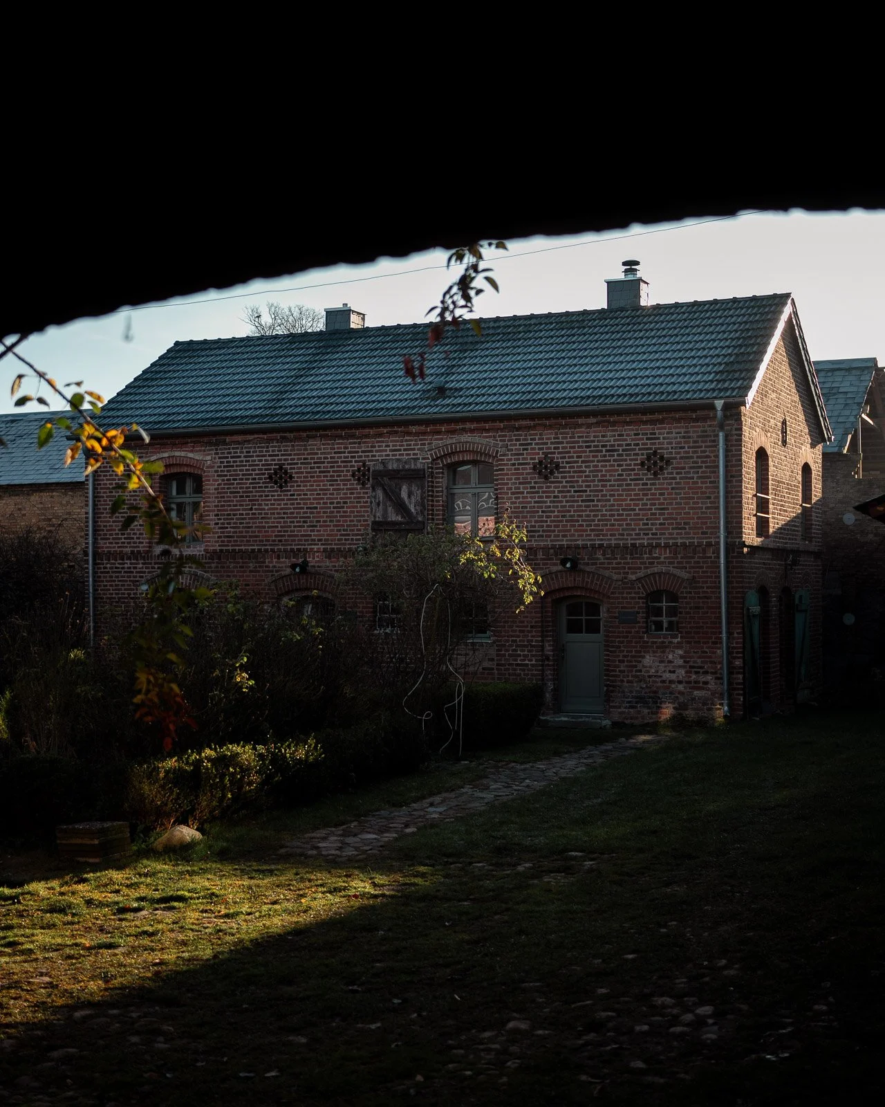 Ein altes Backsteinhaus mit grauem Dach, gesehen durch eine dunkle Öffnung, mit Garten im Vordergrund.