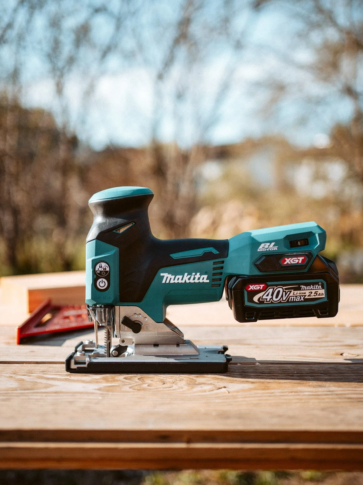 Akku-Stichsäge von Makita auf einem Holztisch, Hintergrund mit Bäumen im Freien, weiches Sonnenlicht.