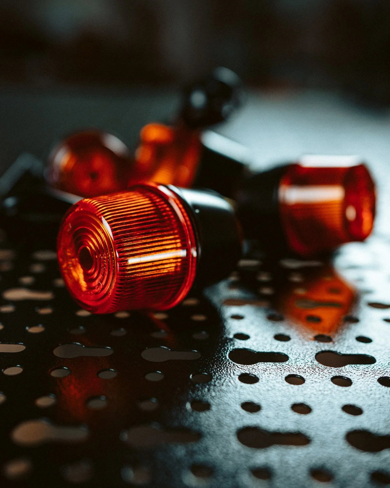 Rote Blinklichter liegen auf einer schwarzen, gelochten Oberfläche, mit Wasserflecken.