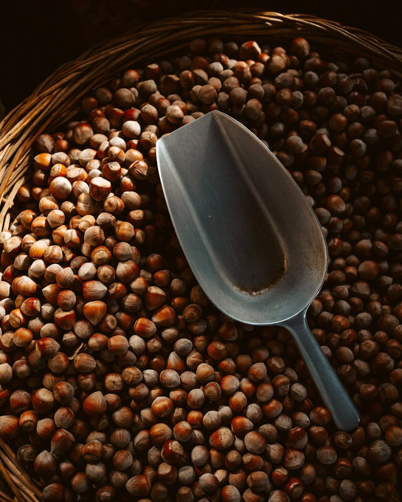Eine große Schale voller Haselnüsse mit einem Metalllöffel, der eine dunkle Flüssigkeit enthält.