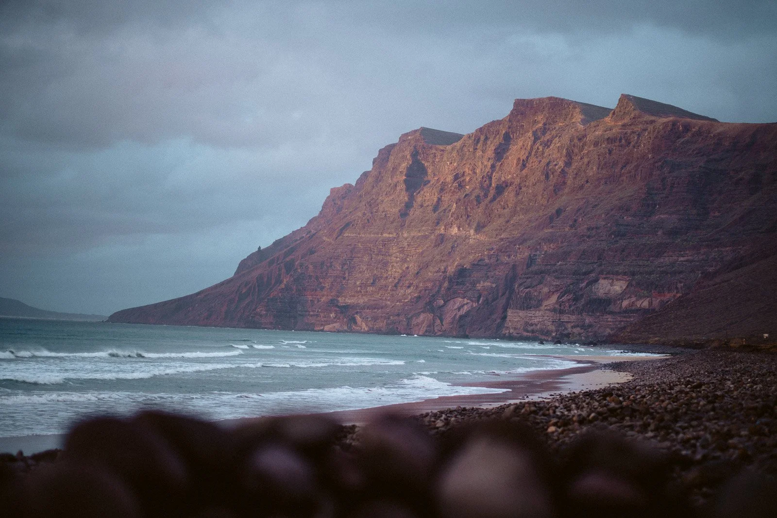 Hügel mit schroffen Felsen an einem einsamen Strand bei bewölktem Himmel