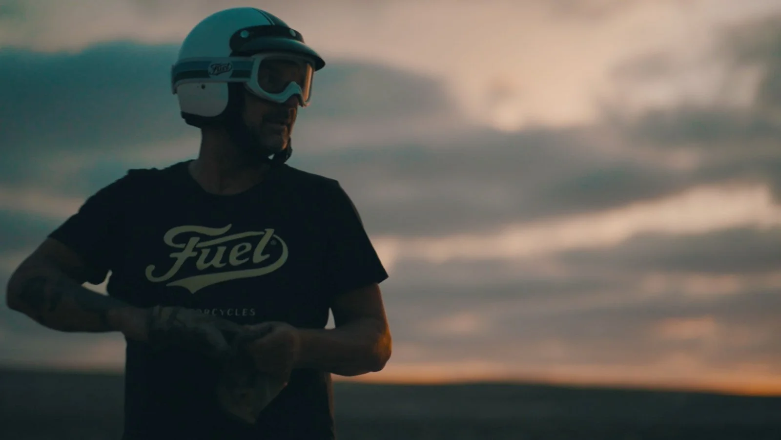 Mann trägt einen Helm und eine T-Shirt mit der Aufschrift 'Fuel' gegen einen Himmel im Sonnenuntergang.
